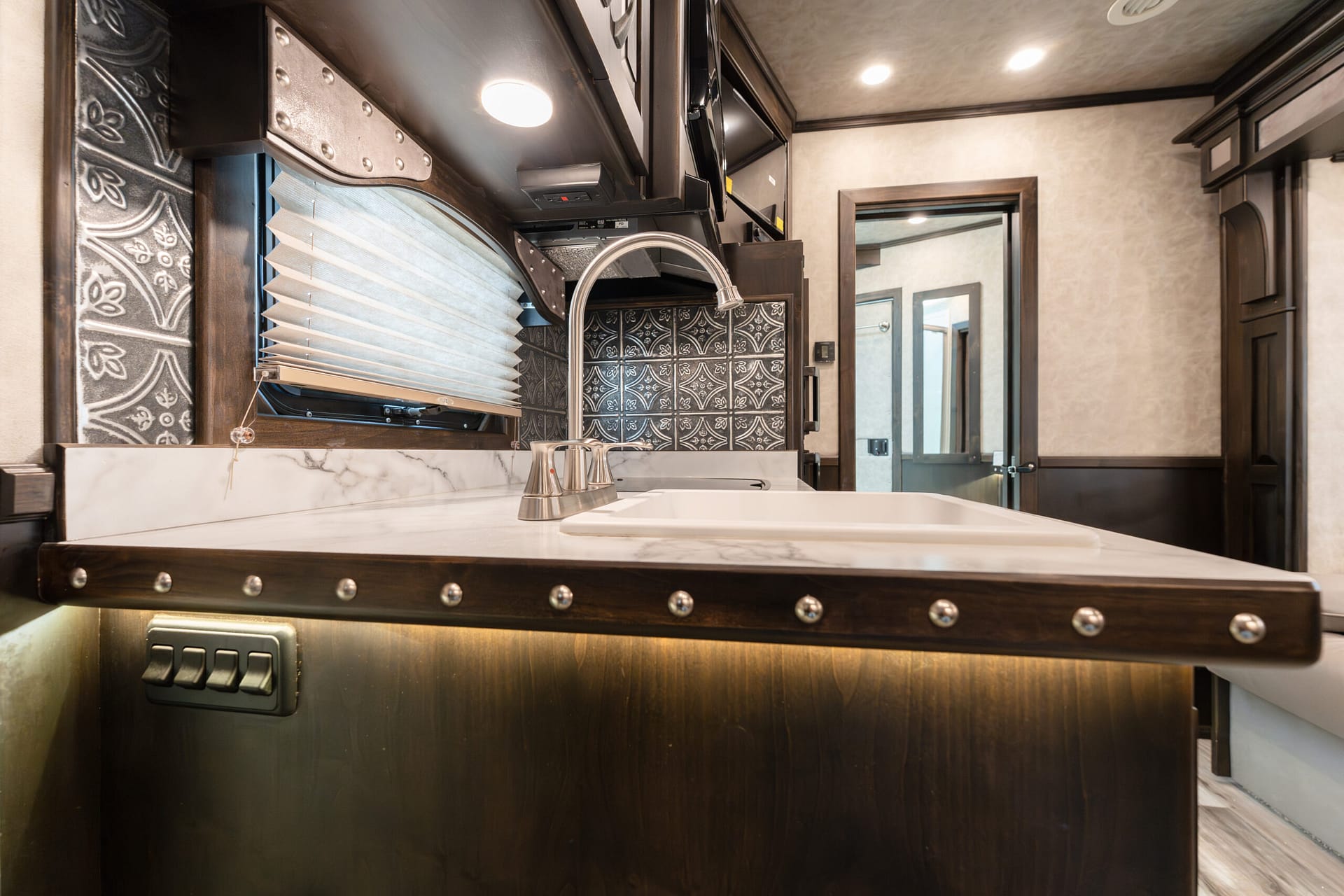RV kitchen counter with white sink, curved chrome faucet, dark wood cabinets, and decorative tiled backsplash.