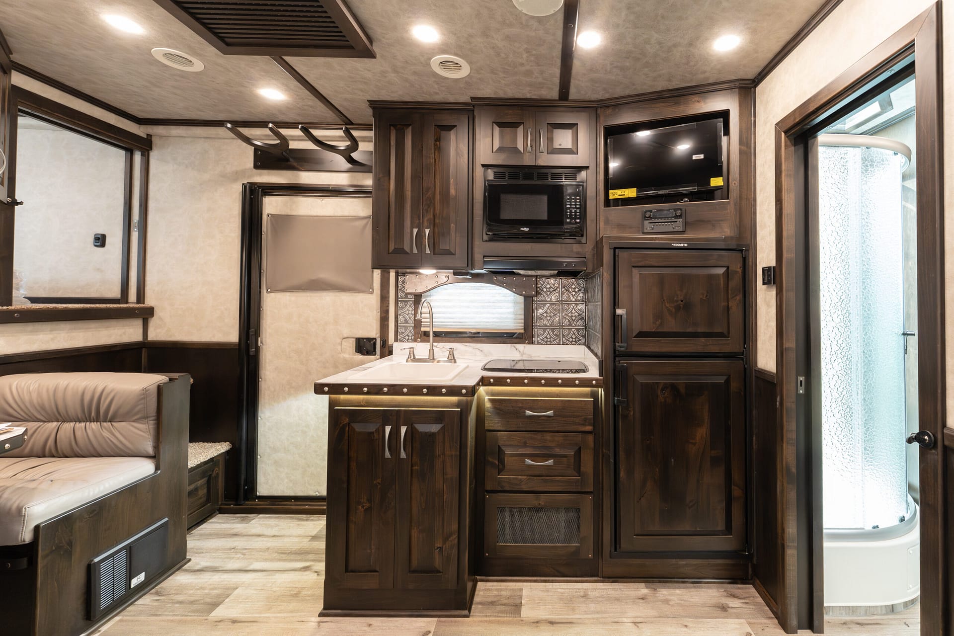 Dark-wood RV kitchen with built-in microwave, oven, and optional TV above, and a central island sink area