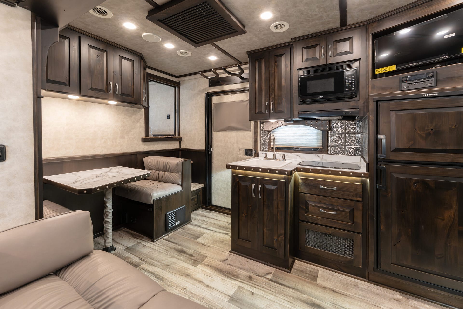 Dark wood RV kitchen and dining area with marble countertops, bench seating, and overhead cabinets.