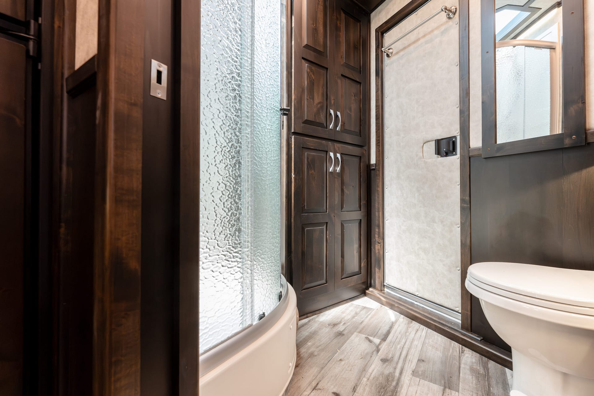RV bathroom featuring a curved glass shower, dark wood cabinets, frosted glass panel, and a white toilet in a compact space