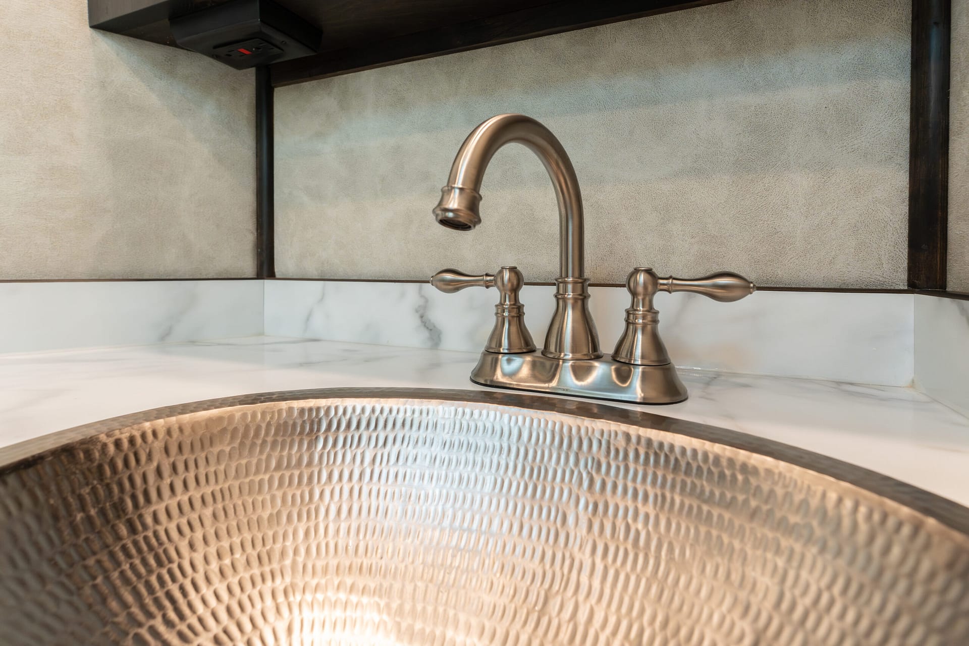 Close-up of a brushed-nickel kitchen faucet with a curved spout above a hammered metal sink.
