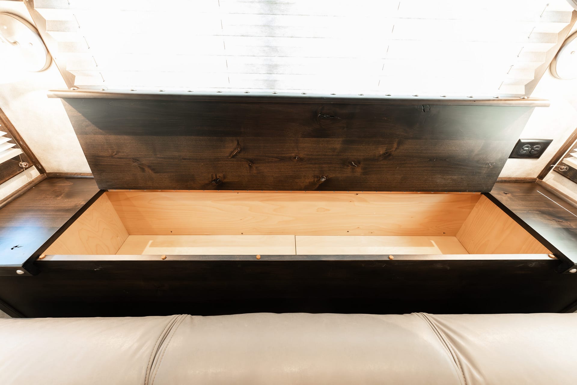 Open storage compartment under a dark wooden bed frame with light wood trim and beige upholstery.