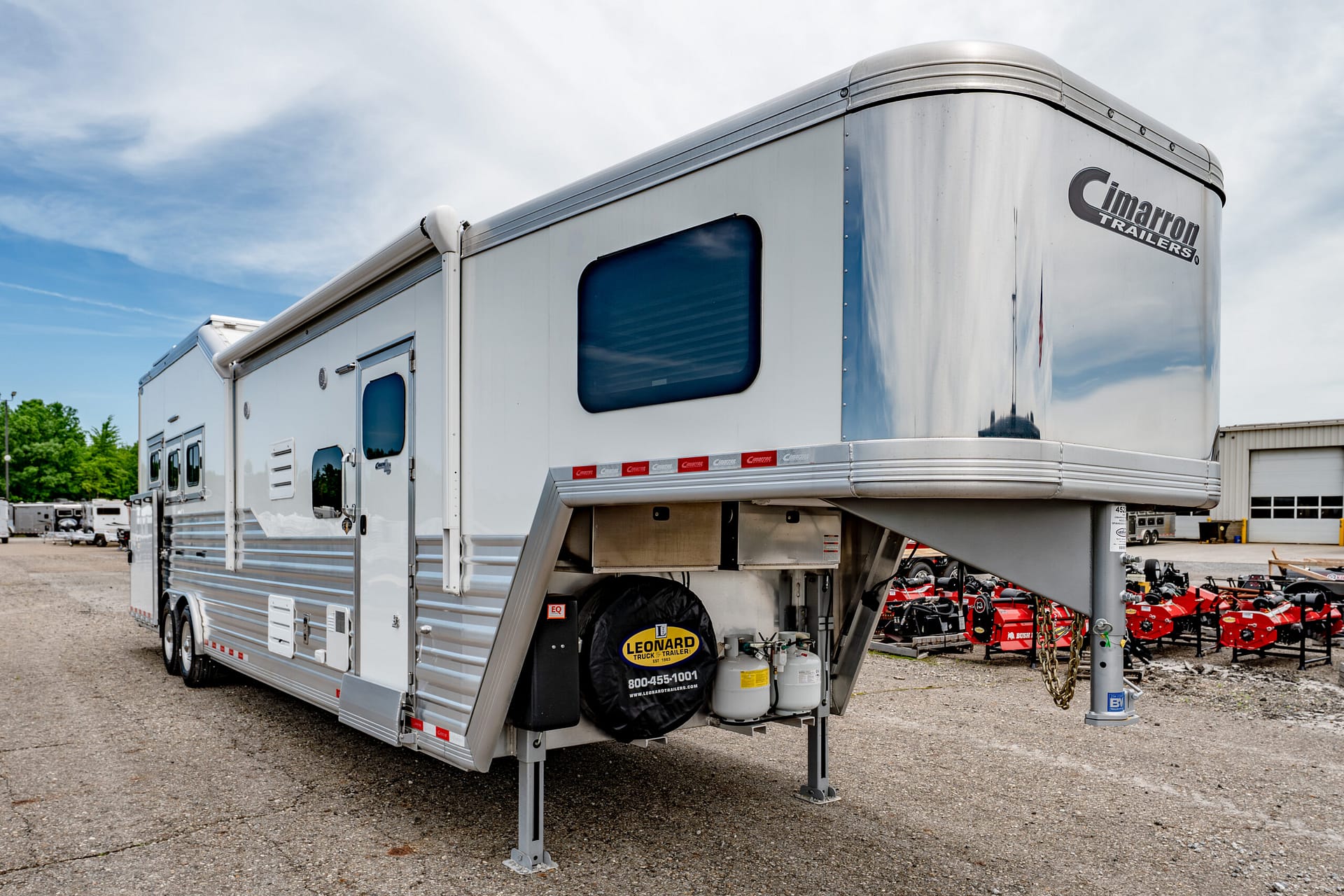 Silver Cimarron gooseneck trailer with stabilizer legs extended in a lot.