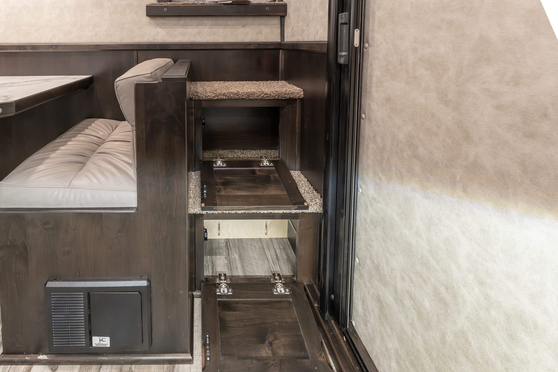 Interior of a dark wood RV with a cushioned bench seating and a hidden carpeted staircase/storage under a pull-out compartment