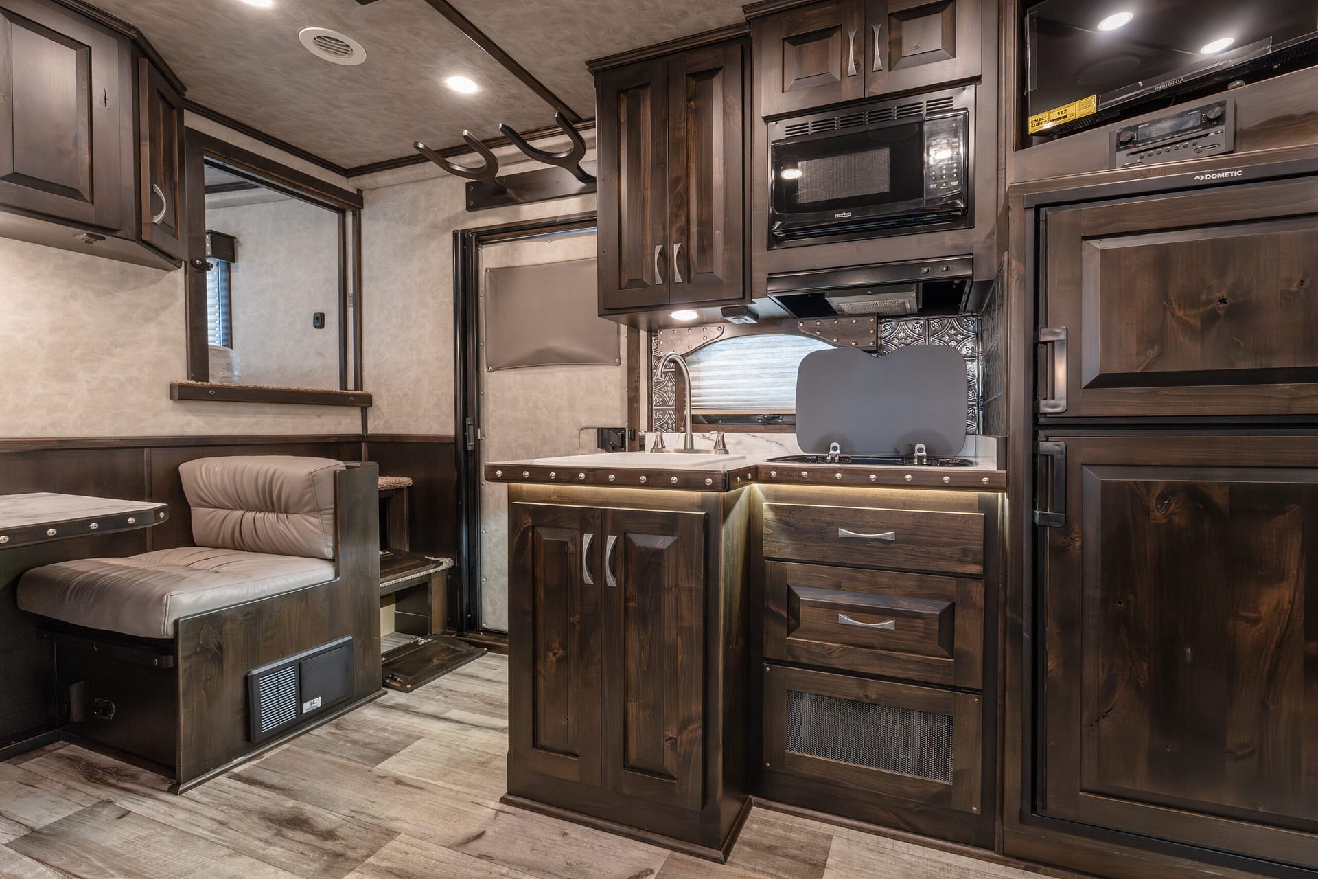 Interior of a dark wood RV kitchen with built-in microwave, oven, and metal backsplash area creating a compact, functional galley area