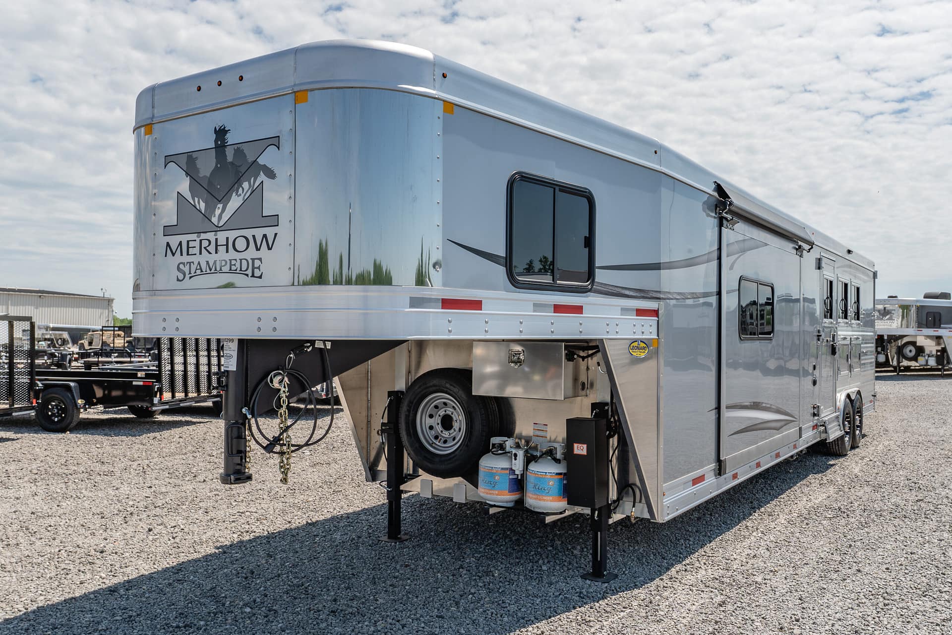 Silver Merhow Stampede horse trailer with logo on the front, parked on a gravel lot.