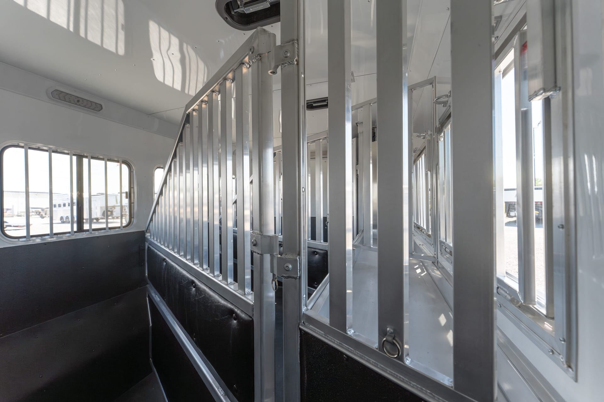 Interior of an empty metal trailer with vertical divider bars and dark flooring, light from windows on the left side.