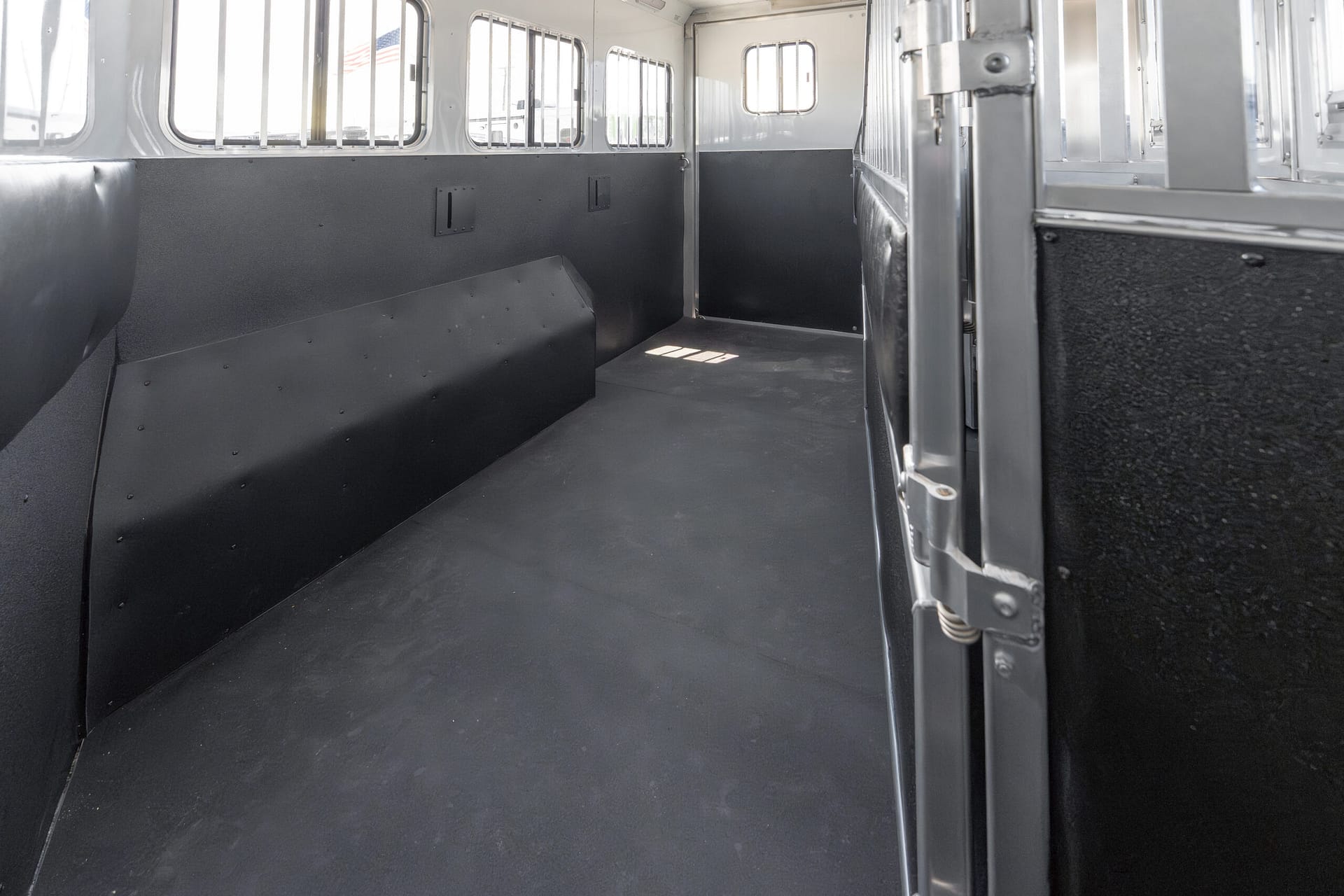 Empty transport interior with dark metal walls, black paneling, and barred windows along the left side of a vehicle interior.