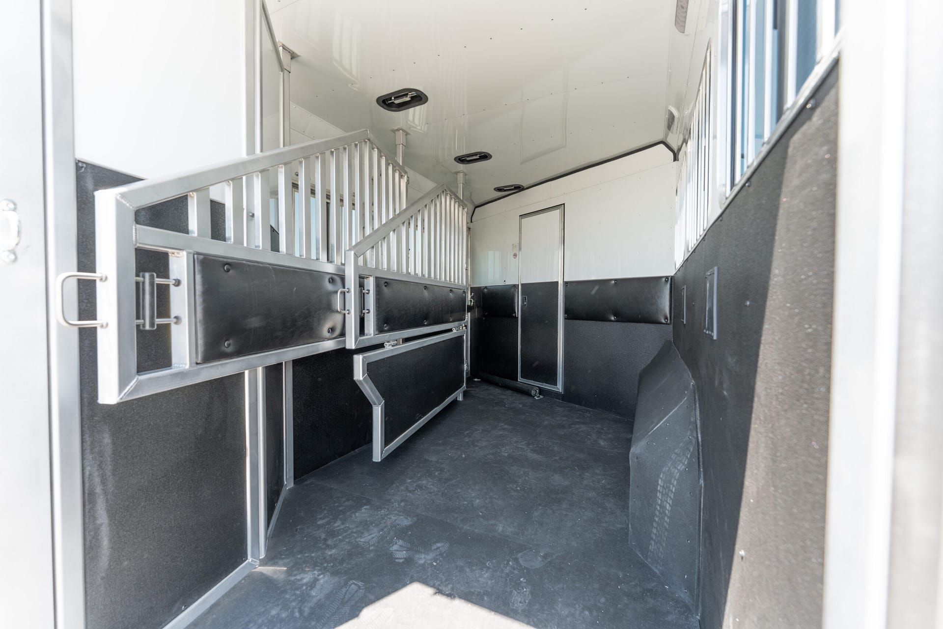 Inside a horse trailer showing partitioned stalls, metal rails, and black padded walls.