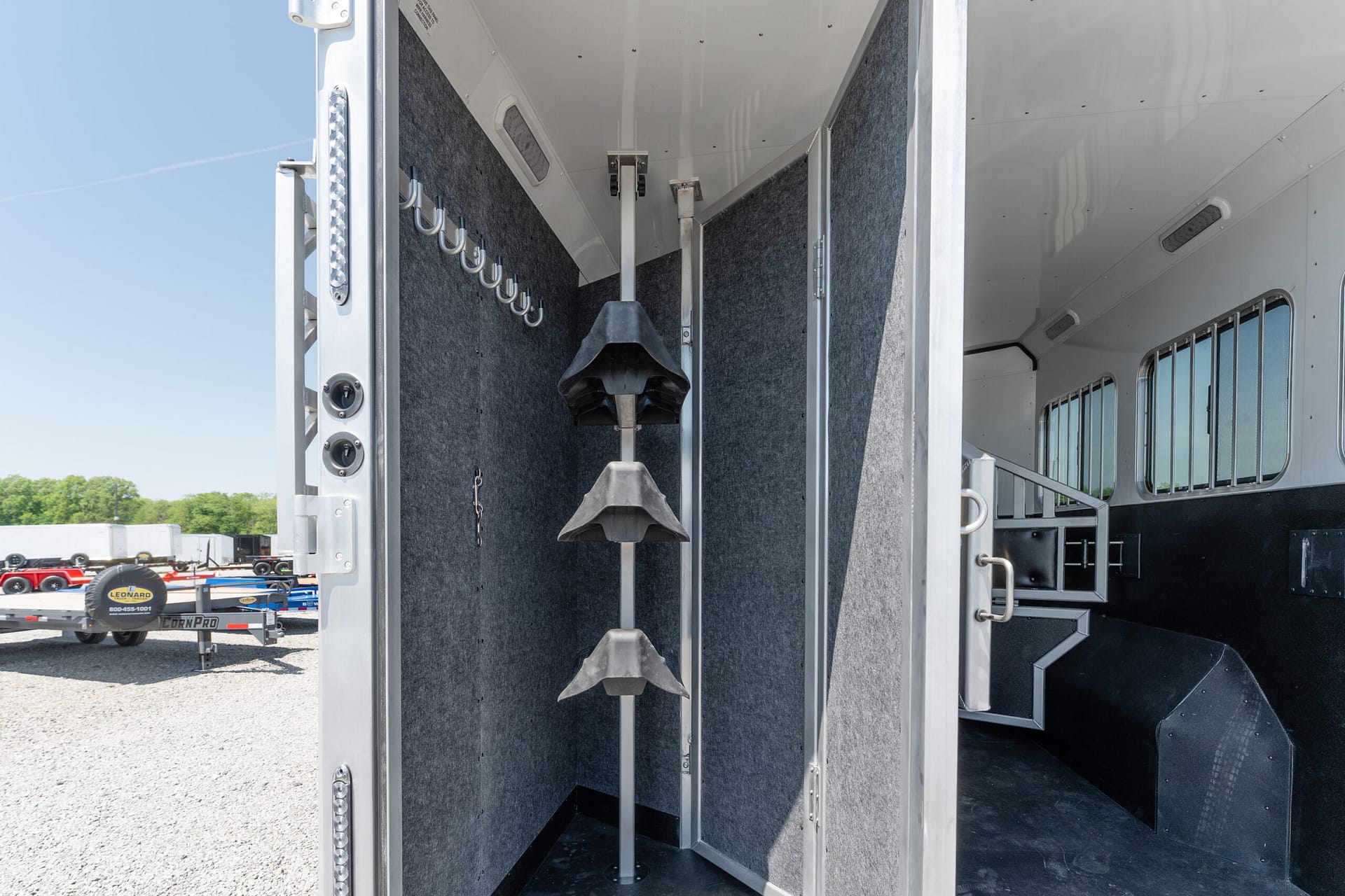 Interior of a horse trailer with a central metal stepped ramp and grey carpeted walls, hooks along the left panel
