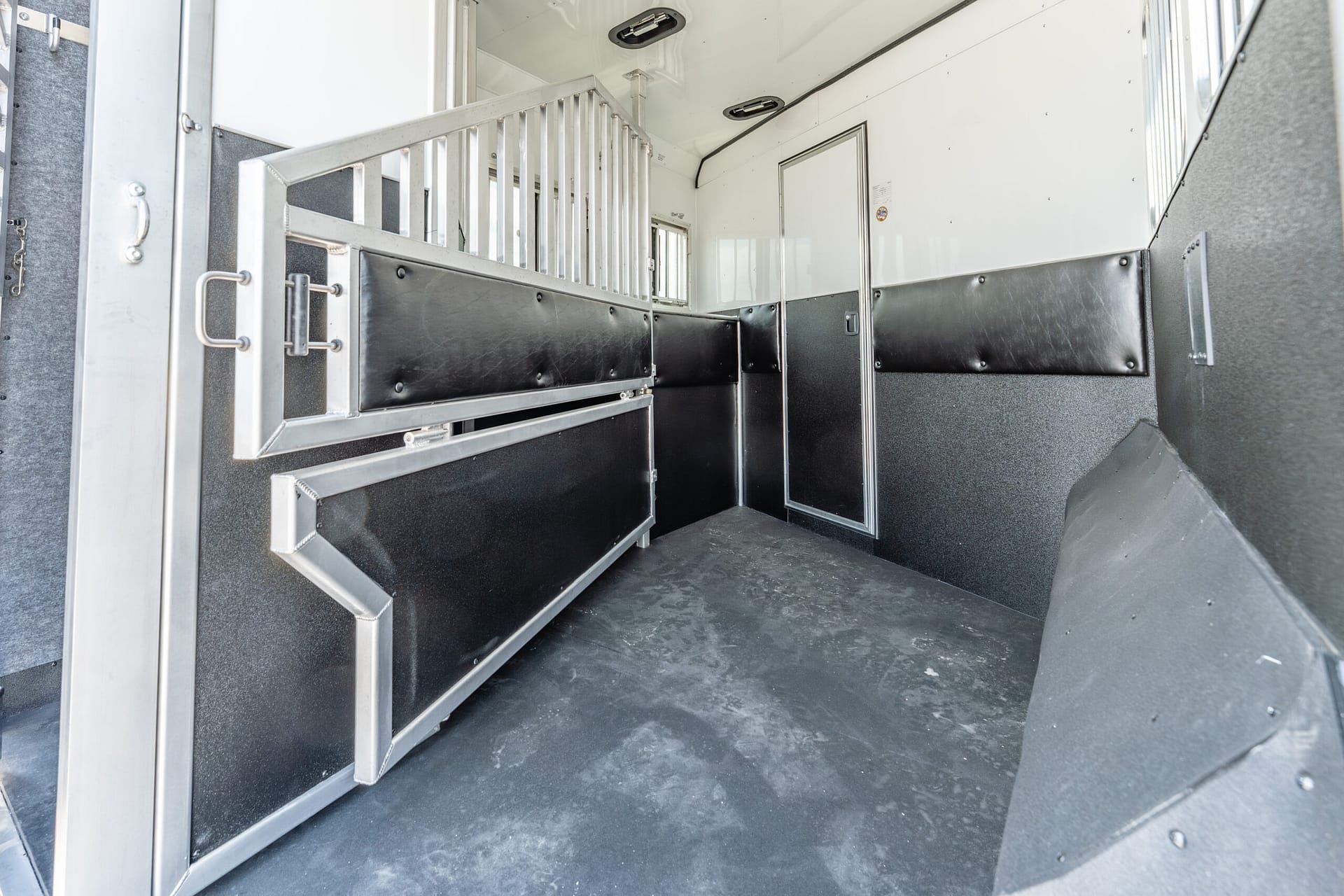 Interior of a metal horse trailer with partitioned stalls, padded black walls, and a rubber floor