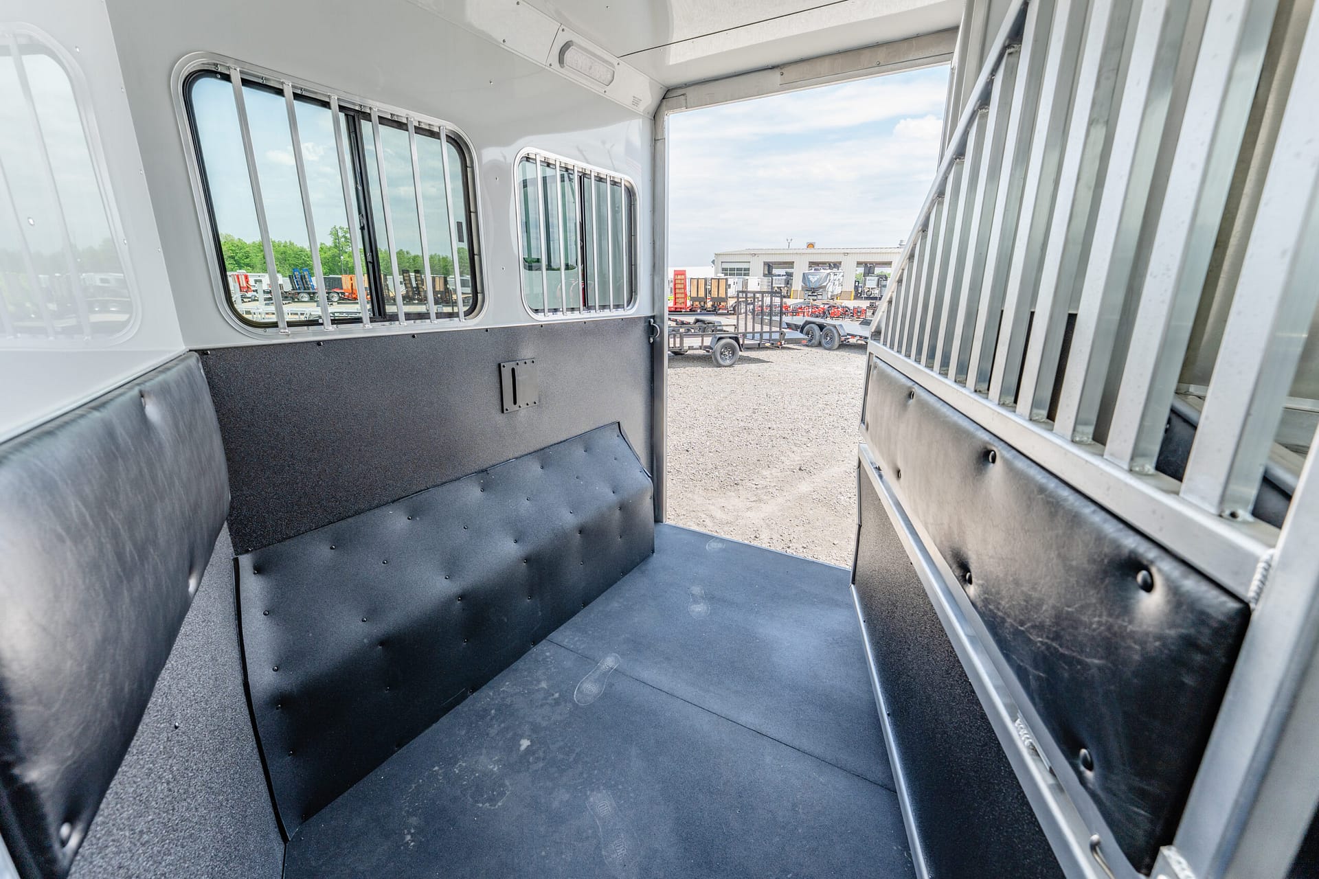 Interior of an empty metal livestock trailer with padded walls and barred windows, looking toward the outdoor loading area.