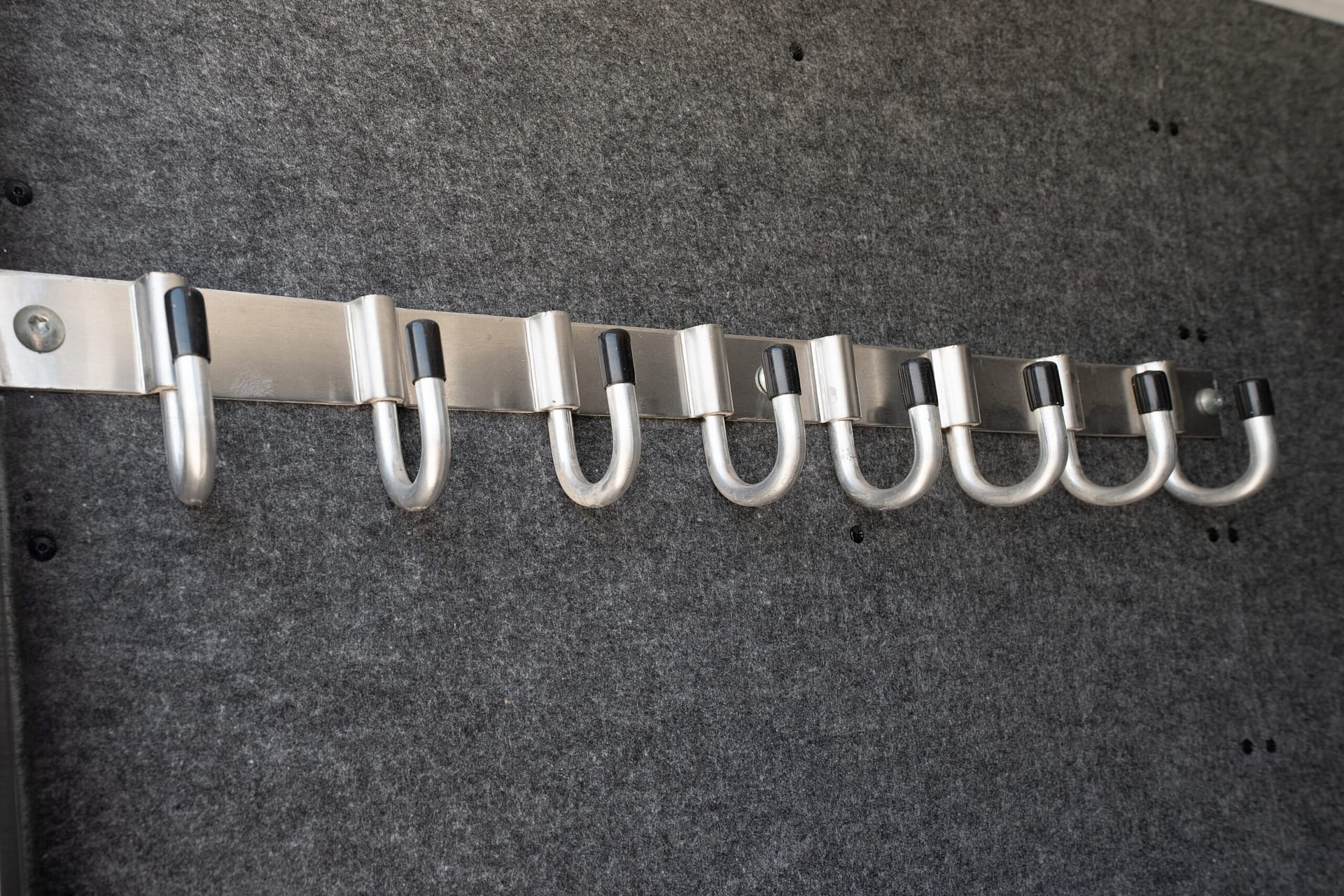 Close-up of a row of silver coat hooks attached to a metal rail on a dark grey felt background with black tips on the hooks