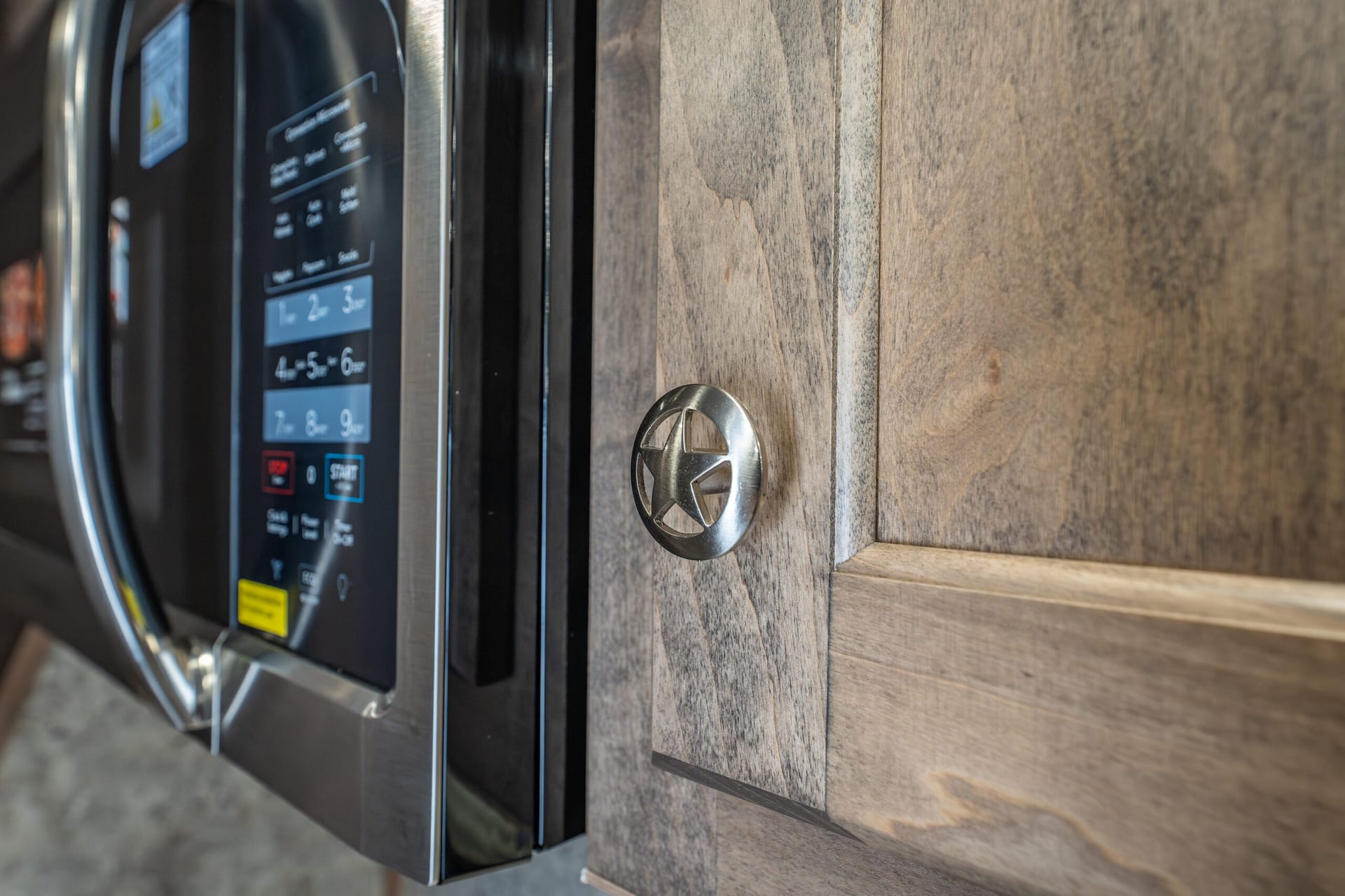 Built-in stainless steel microwave with a round knob and wood cabinetry surrounding it, control panel visible on the left.