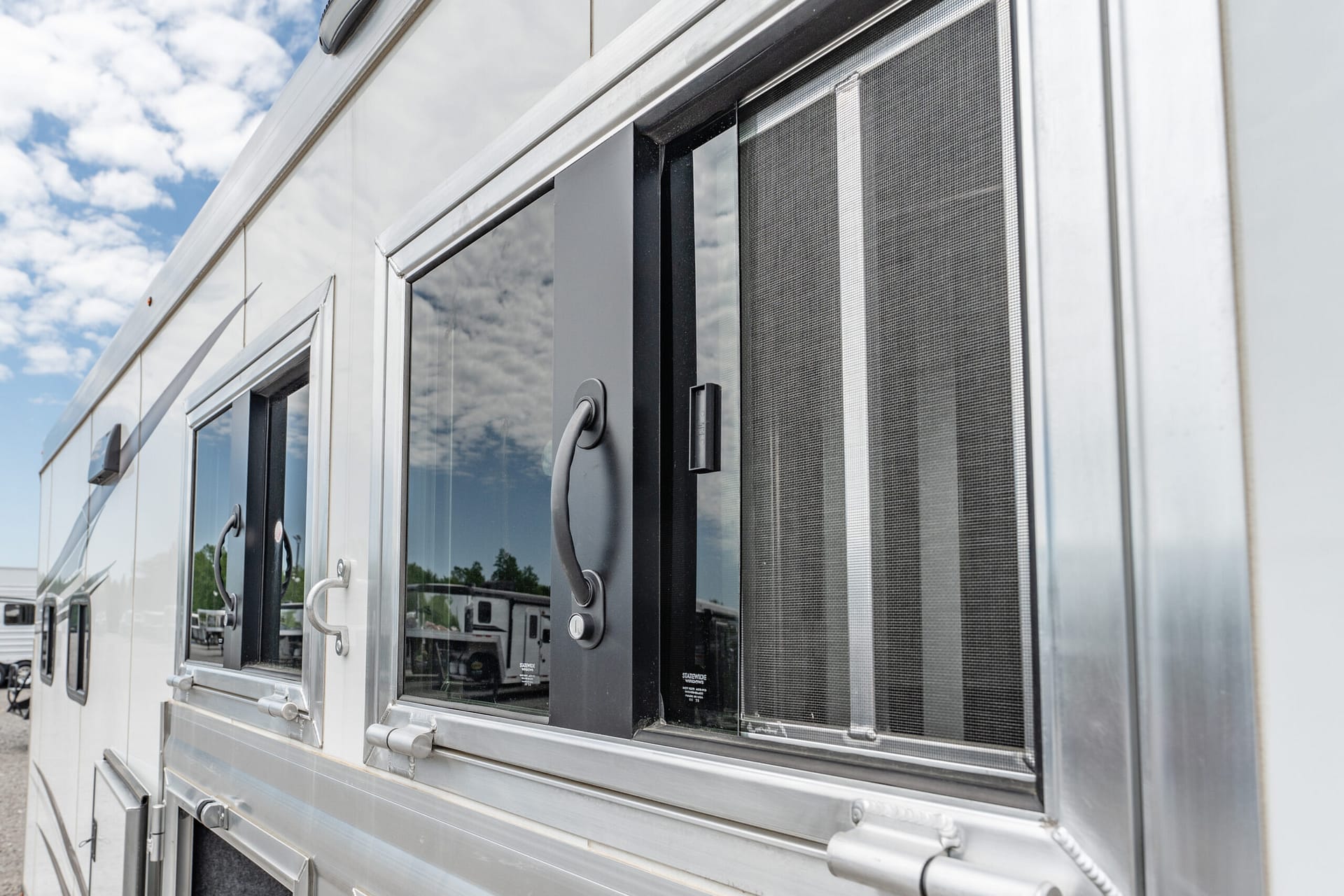 Close-up of a silver aluminum vehicle door with a window and handle, reflecting the blue sky.