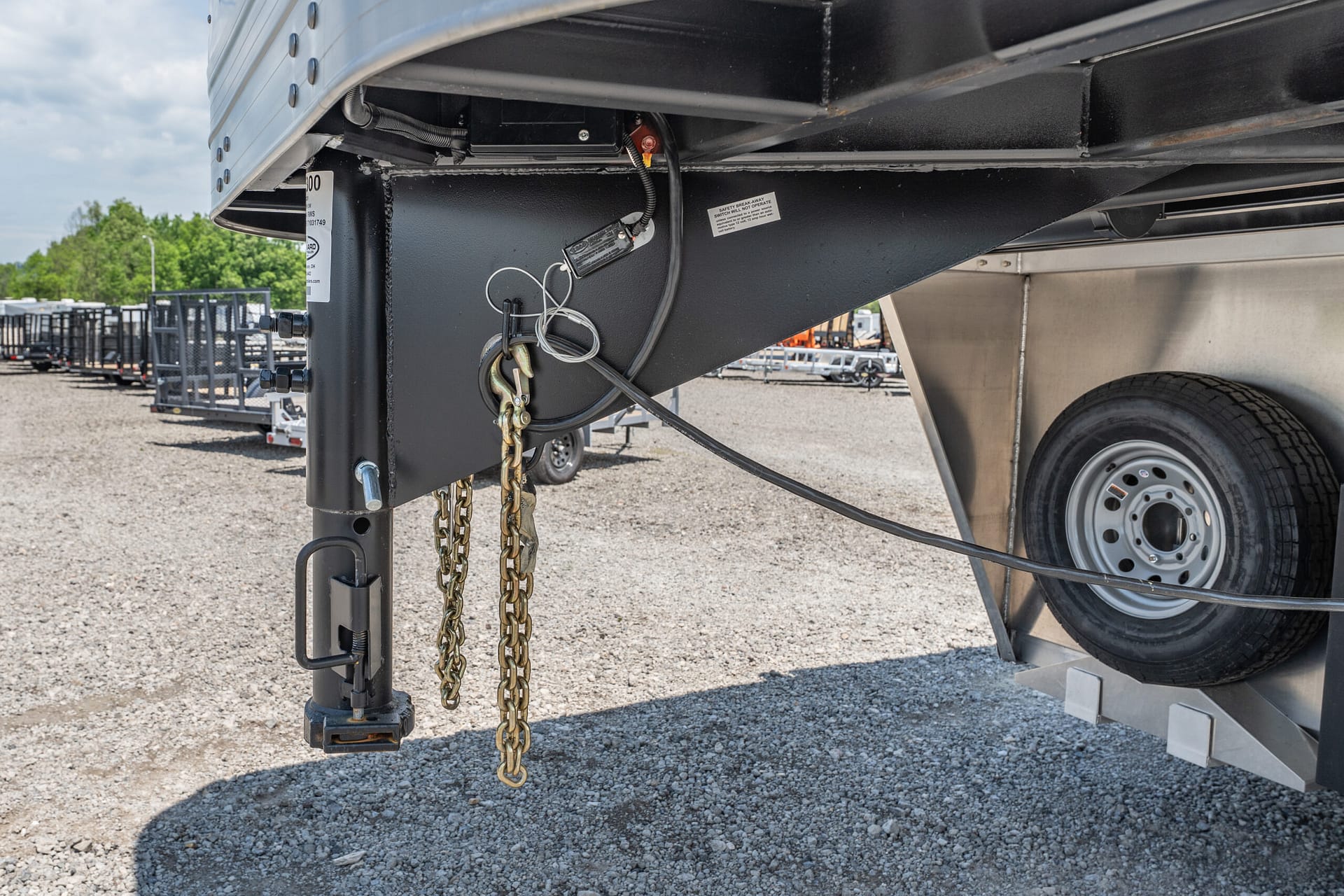 Close-up of a trailer hitch area with safety chains and electrical cables hanging from a black steel frame, spare wheel visible in the background