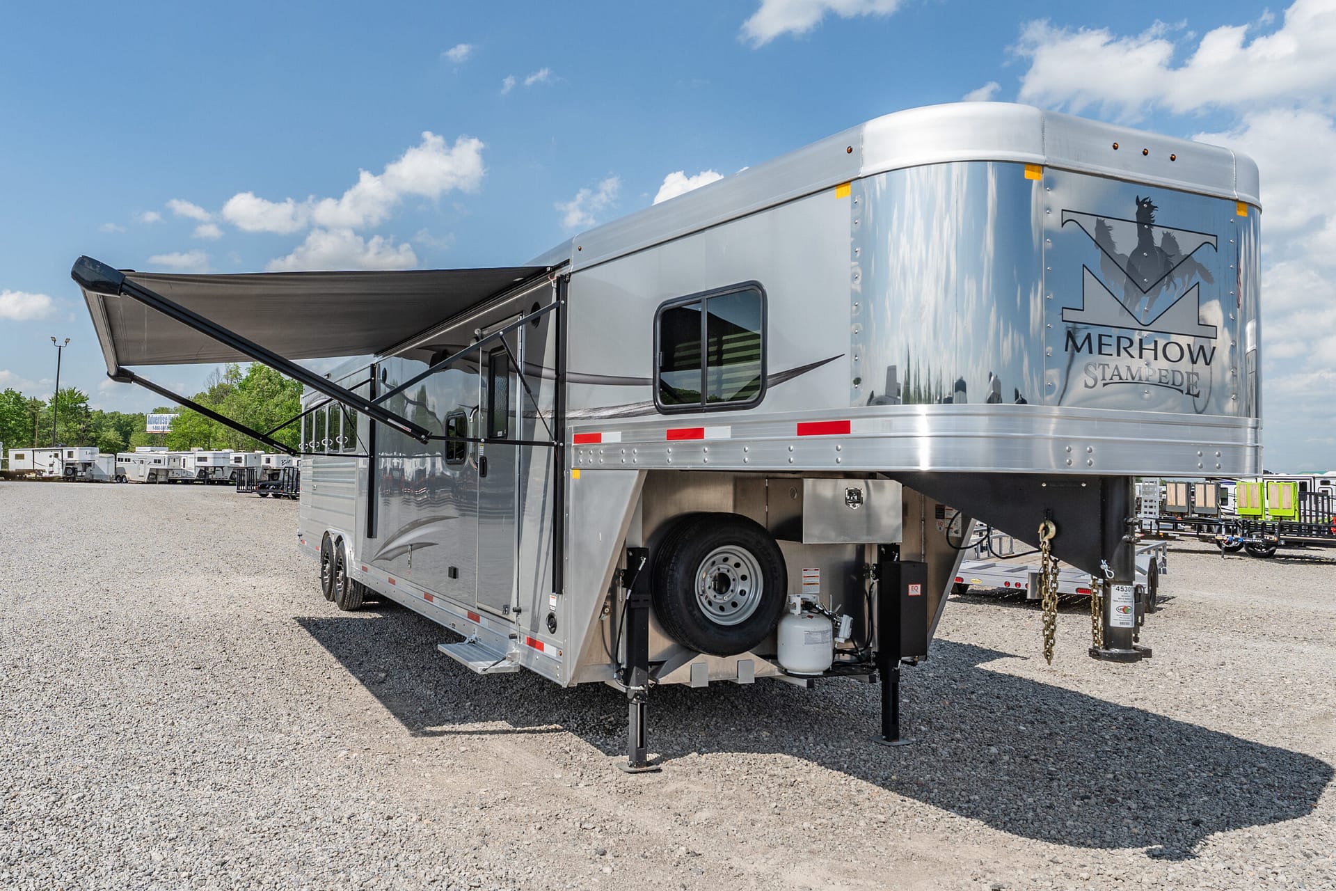 Shiny Merhow Stampede horse trailer with extended awning in a gravel lot.