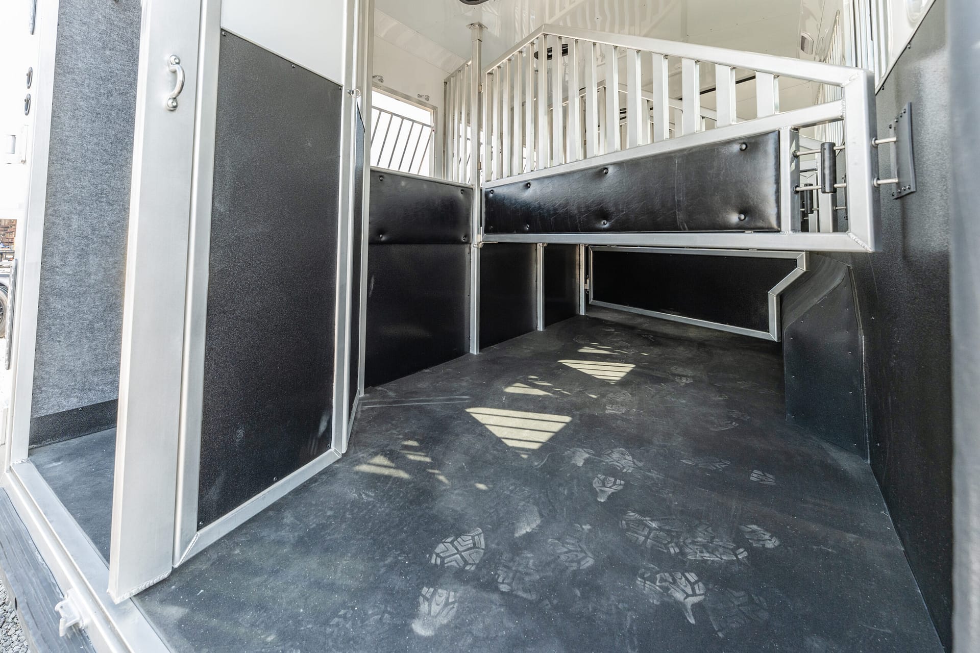 Interior of a horse trailer with partitioned stalls, black padded walls, and metal rails.