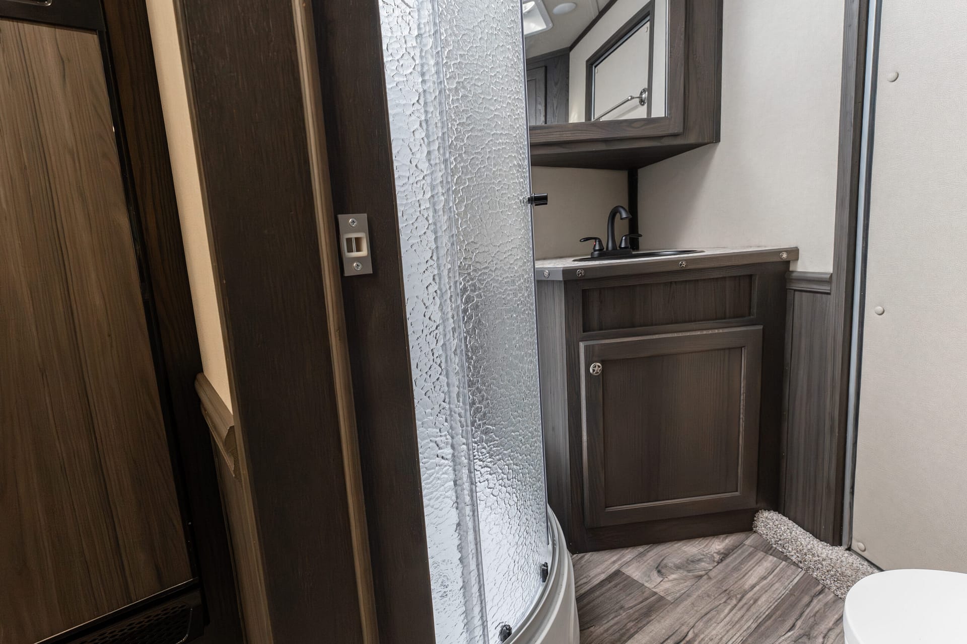 RV bathroom interior with dark wood vanity, frosted textured shower door, and mirror above sink area