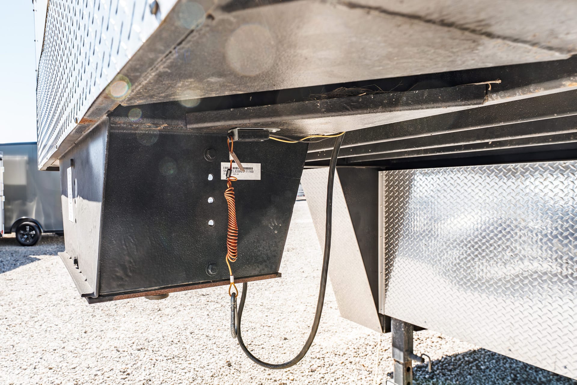 Close-up of the underside of a utility trailer showing a black metal frame, hanging wires, and an orange coiled cord.