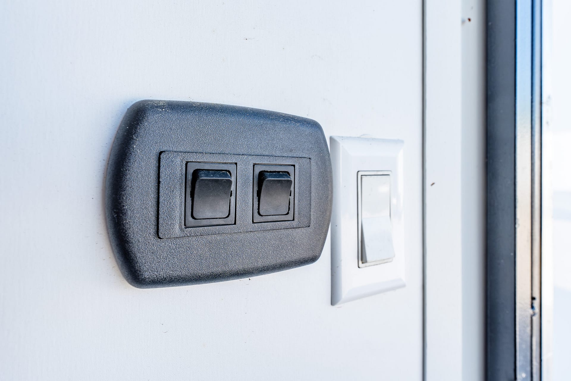 Close-up of a black plastic dual rocker switch on a light-colored surface, with a separate white toggle switch nearby on the door frame.