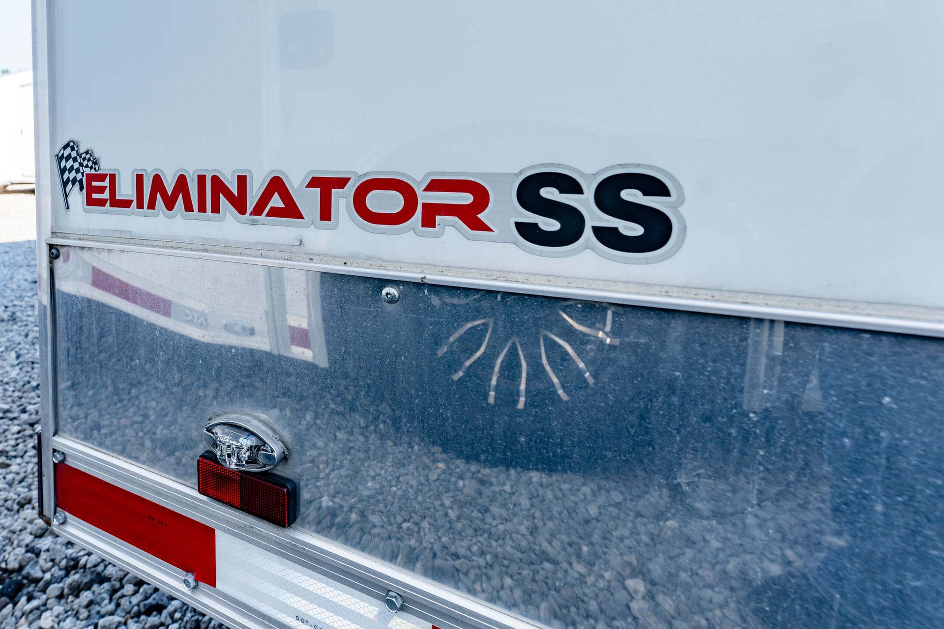 Rear of a white trailer showing 'ELIMINATOR SS' logo in red and black with a checkered flag graphic on the side edge.