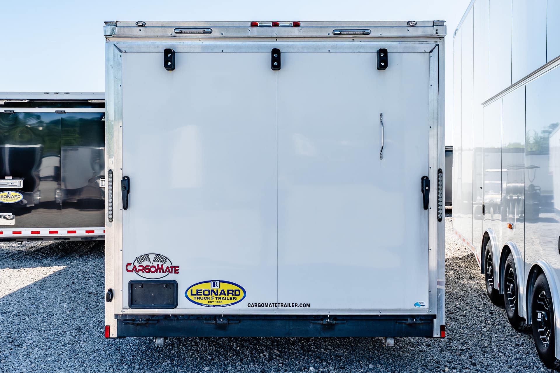 Rear view of a white cargo trailer with closed doors, door latches, and visible logos for CARGOMATE and LEONARD TRUCK & TRAILER on the back panel.