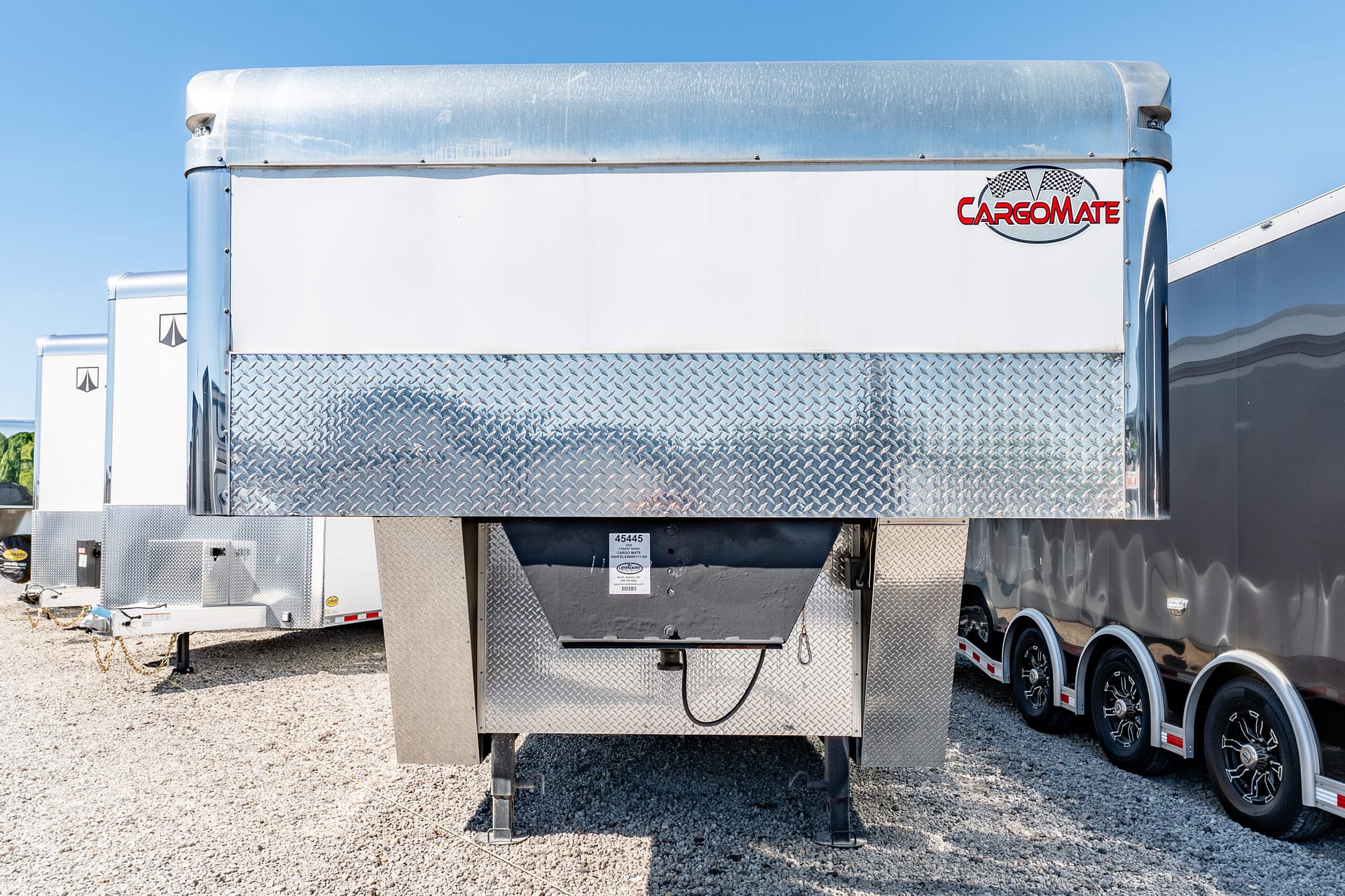 Front view of a white cargo trailer with a diamond-plate lower panel, chrome top, and the CARGOMATE logo against a clear blue sky