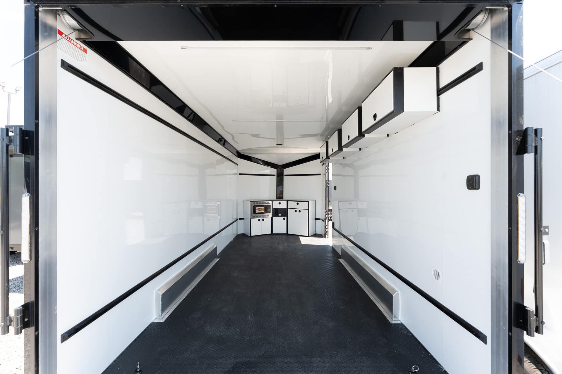 Interior of an empty white cargo trailer with black trim and storage cabinets at the rear, looking toward the back door.