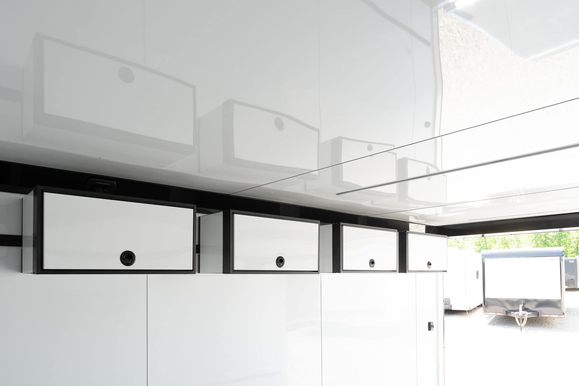 Row of white metal wall-mounted tool cabinets with circular locks in an outdoor industrial area (trailer visible in background).