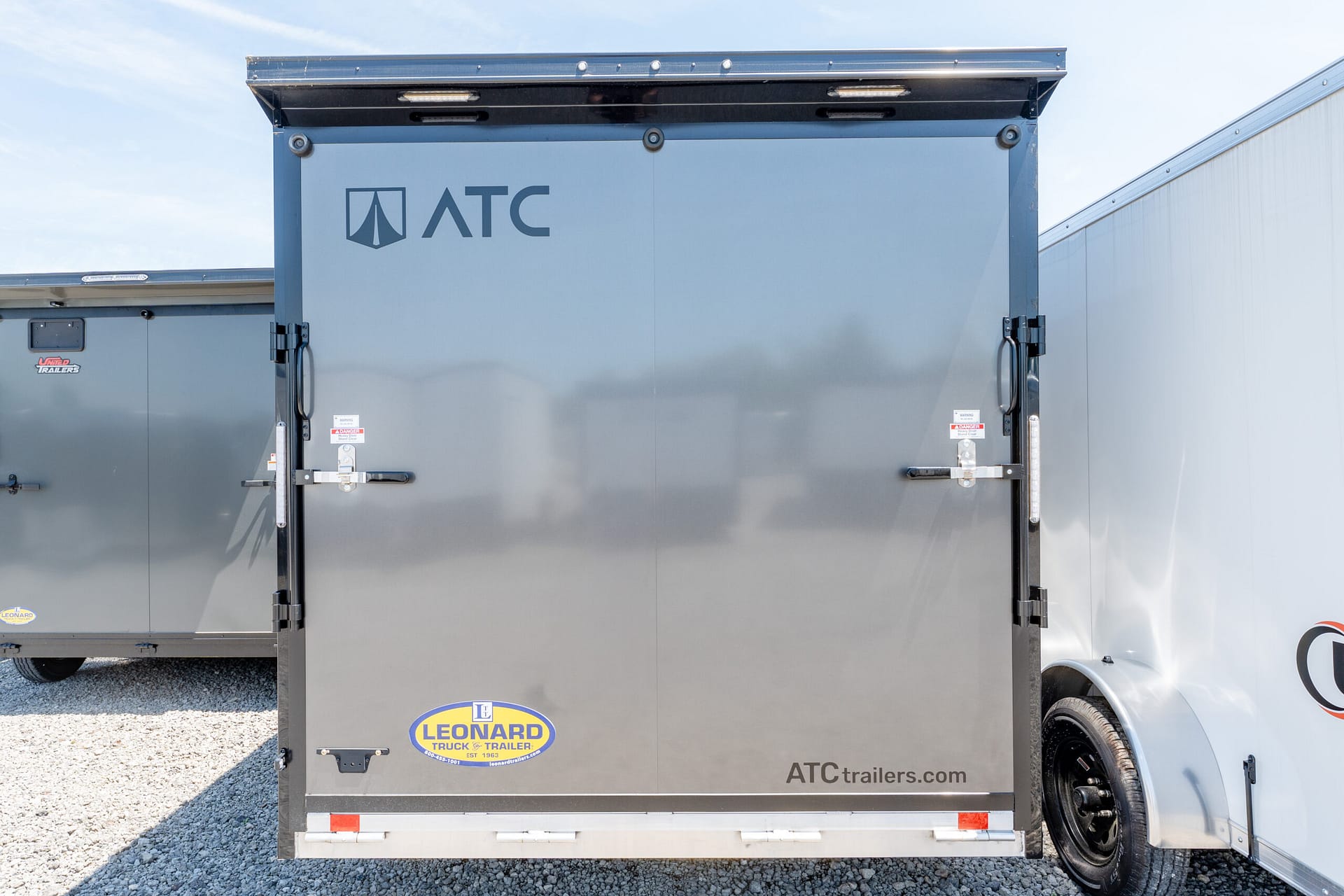Rear view of a gray ATC trailer with closed doors, visible ATC and Leonard logos, parked on gravel.