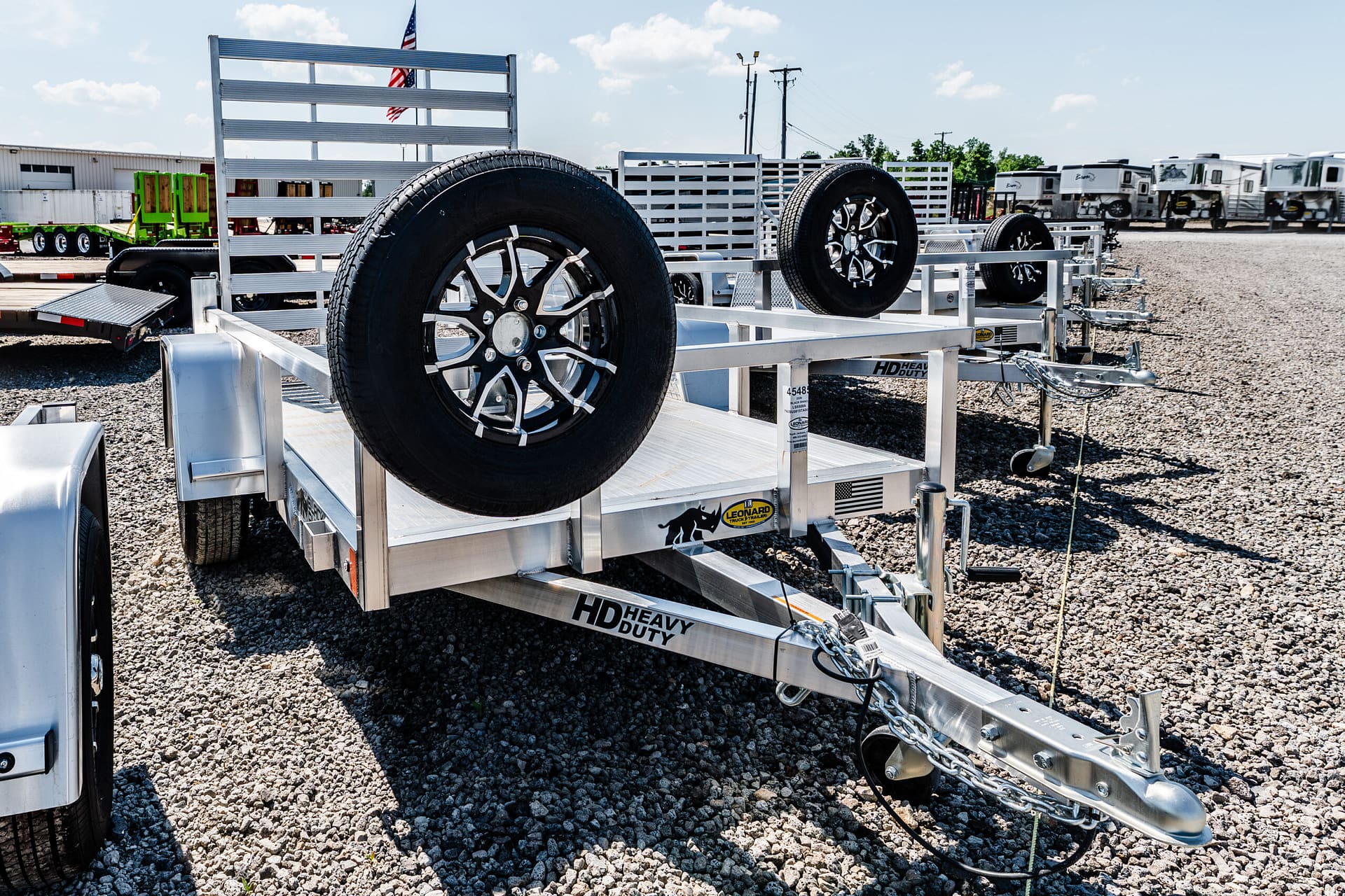 Aluminum trailer with big mounted tires on a gravel lot, other trailers and RVs visible in the background.