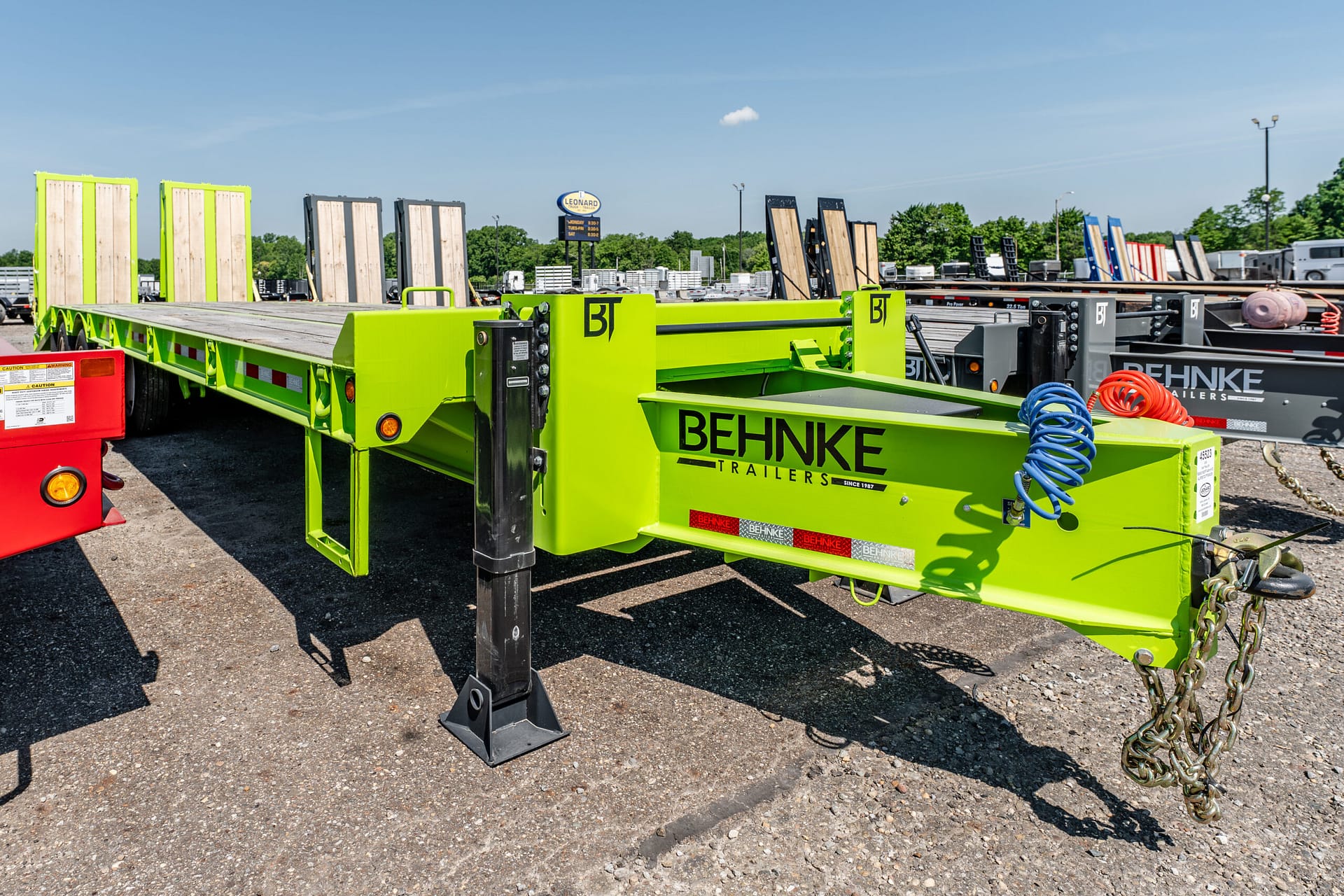 Bright green Behnke trailers flatbed in an outdoor lot with loading ramps and stacked equipment in the background.