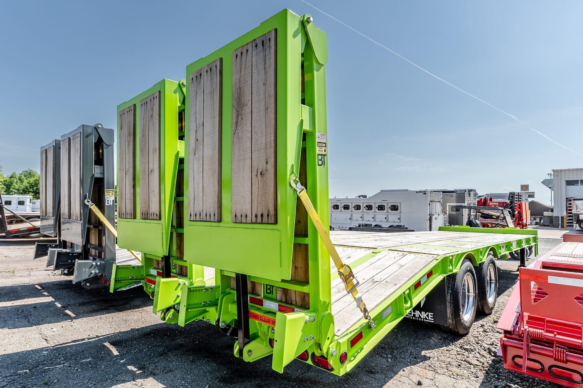 Bright lime-green industrial trailer with wooden plank sides in a truck yard under a blue sky, with other trailers in the background.