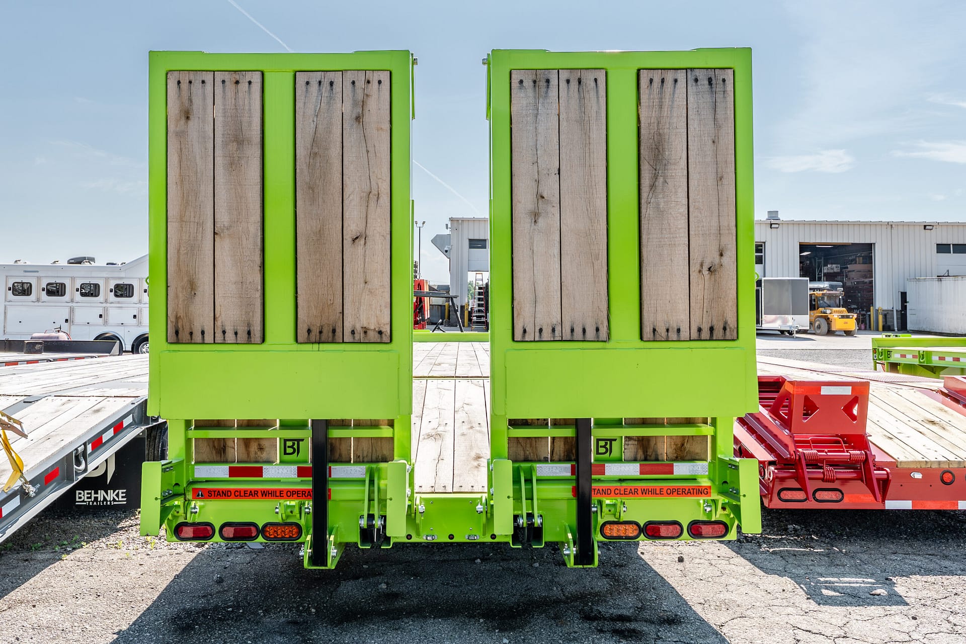 Rear view of a bright green trailer with wood-paneled sides in an outdoor industrial yard.