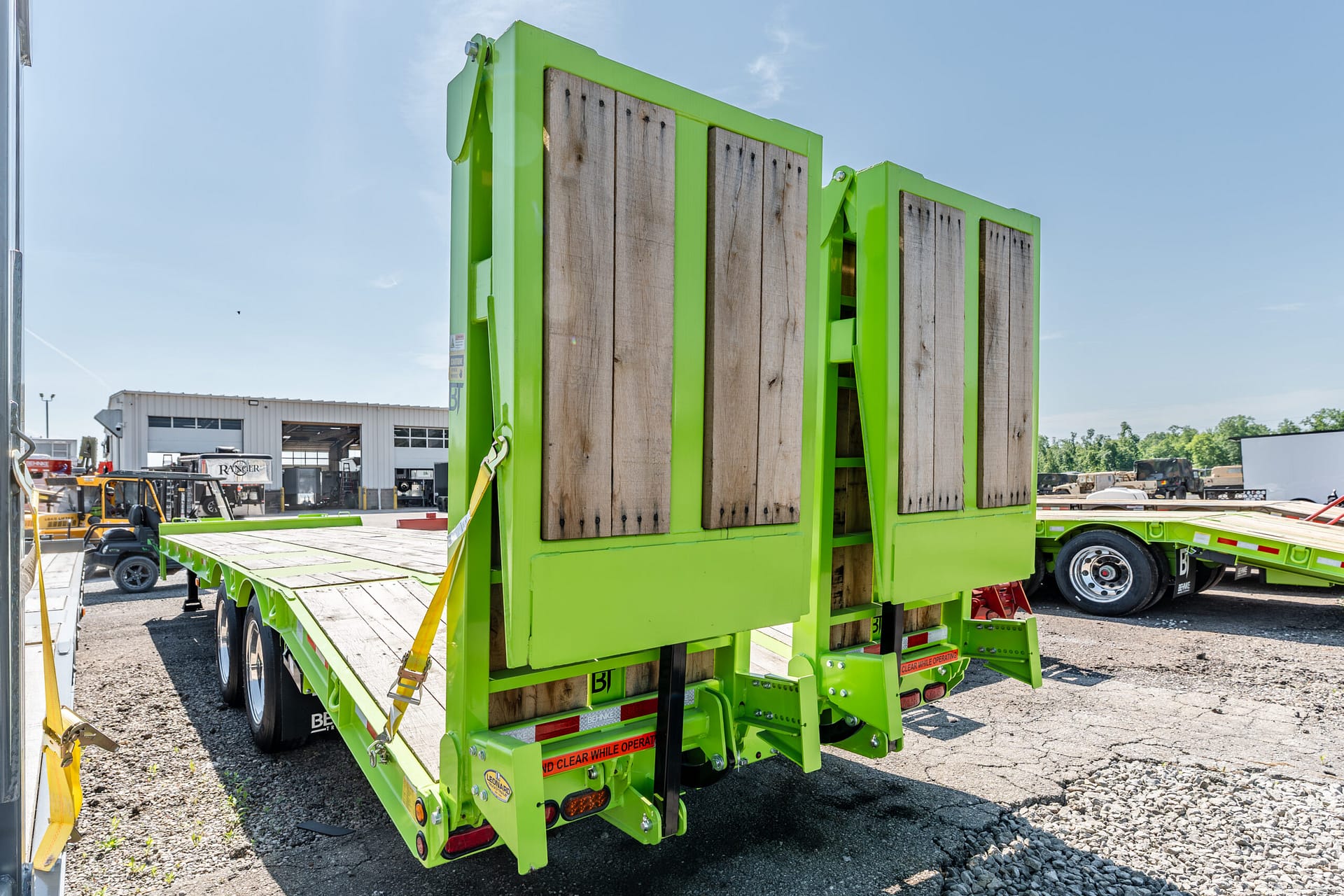Bright green flatbed trailer with wooden side panels in an outdoor industrial yard, loaded and secured with straps.