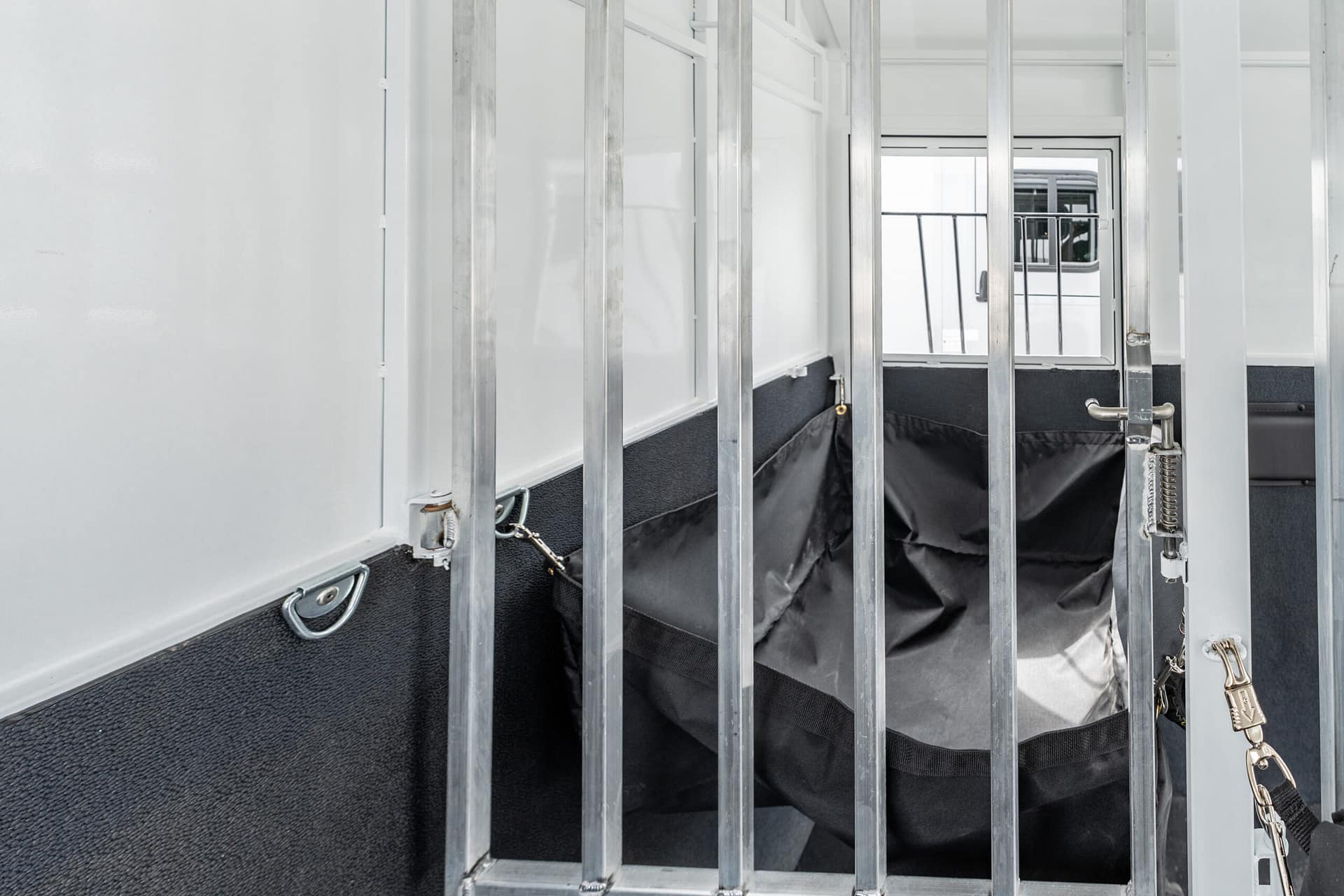 Inside a prison cell with vertical metal bars, a secured door, and a dark padded floor area visible behind the bars.