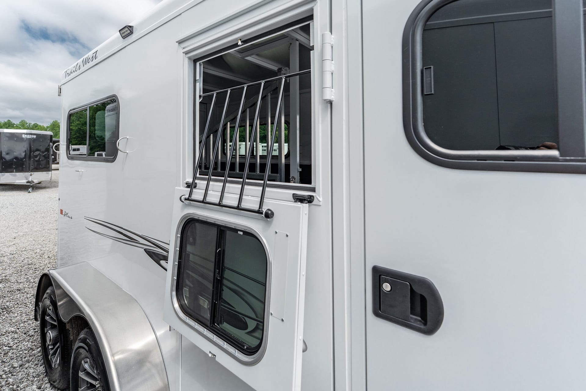 Silver horse trailer side with an open stall window and vertical bars, showing the interior partitions.