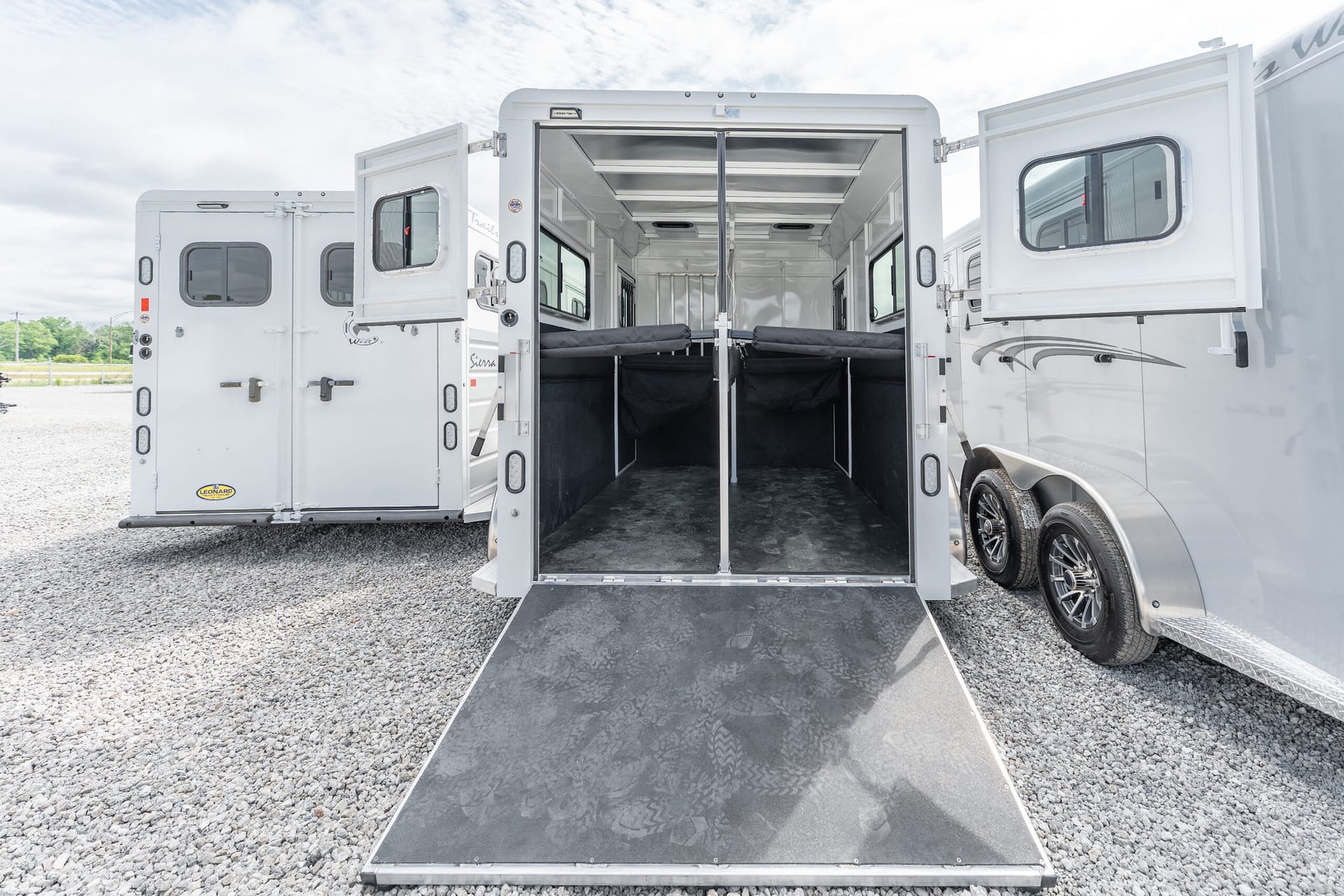 Open horse trailer with rear doors and ramp down, showing partitioned stalls inside for loading horses.