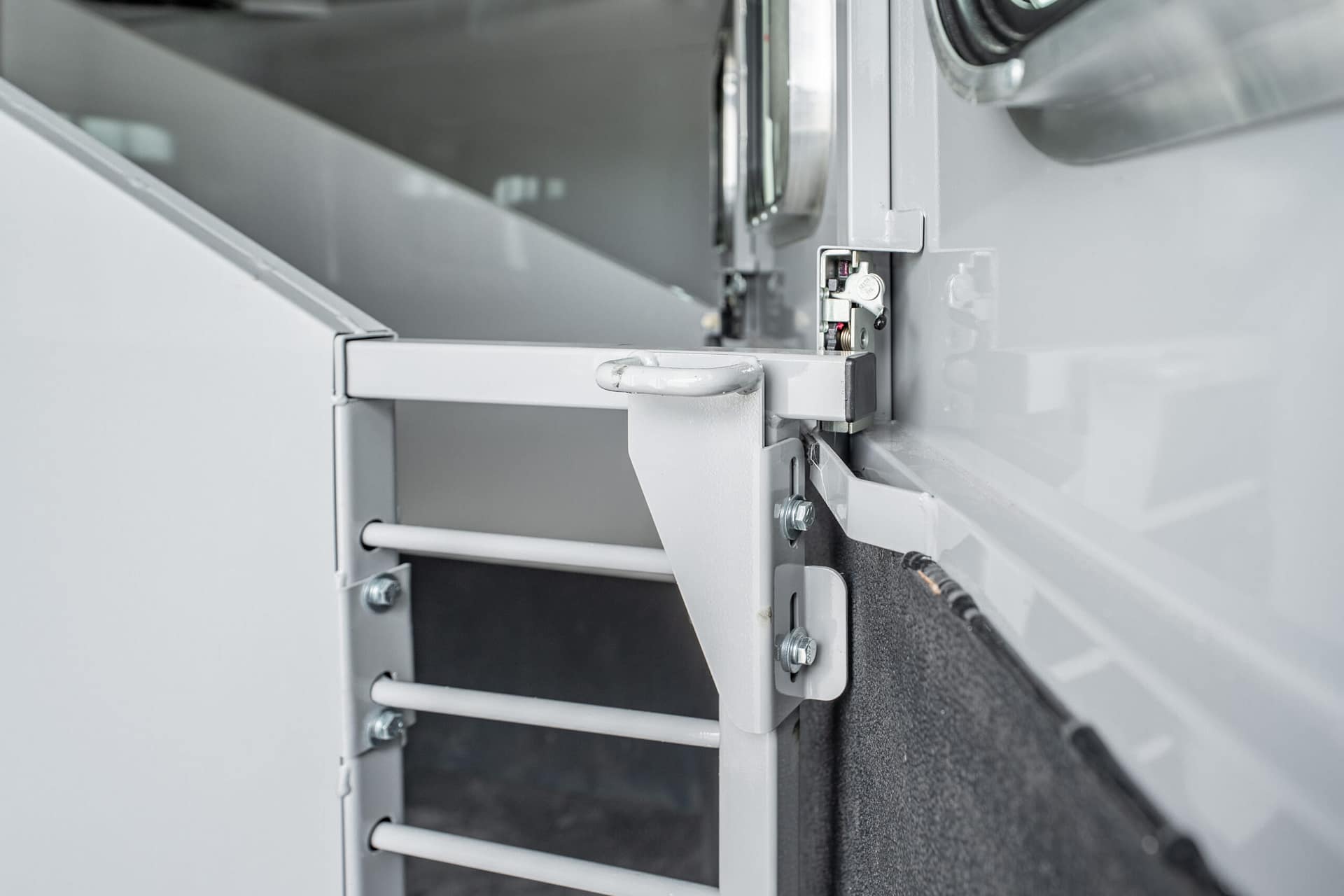 Close-up of a metal cabinet latch and hinge on gray industrial equipment, showing bolts and a securing mechanism.