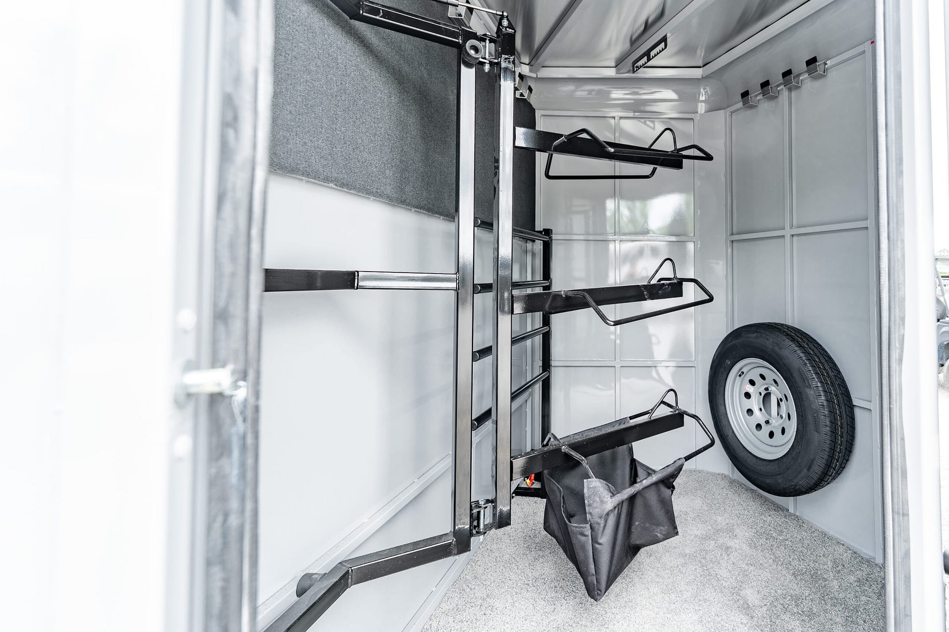 Inside a utility trailer showing metal rack shelving, hanging bars, and a mounted spare tire along the wall