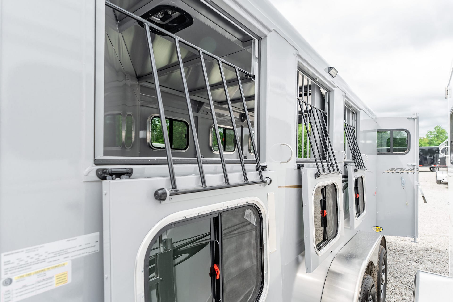 Row of gray horse trailers with barred windows along a gravel lot.