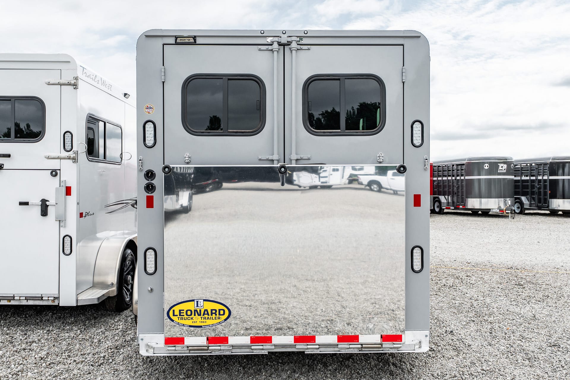 Rear view of a silver semi-trailer with double doors, rounded windows, and a Leonard Truck & Trailer sticker on the bumper area beneath the doors? (informational)