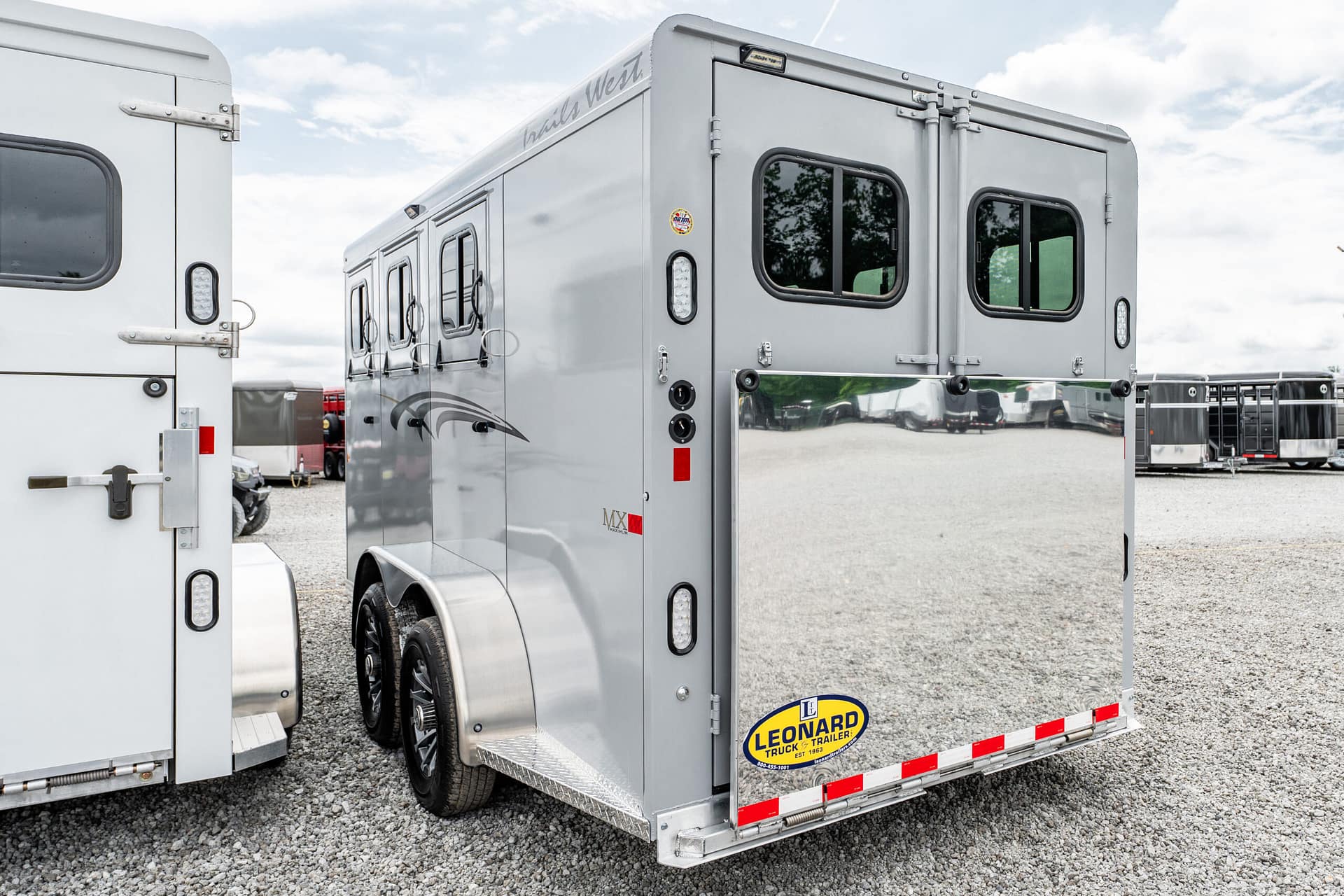 Silver horse trailer close-up showing rear and side doors in an outdoor trailer lot; Leonard logo visible on bumper zone.