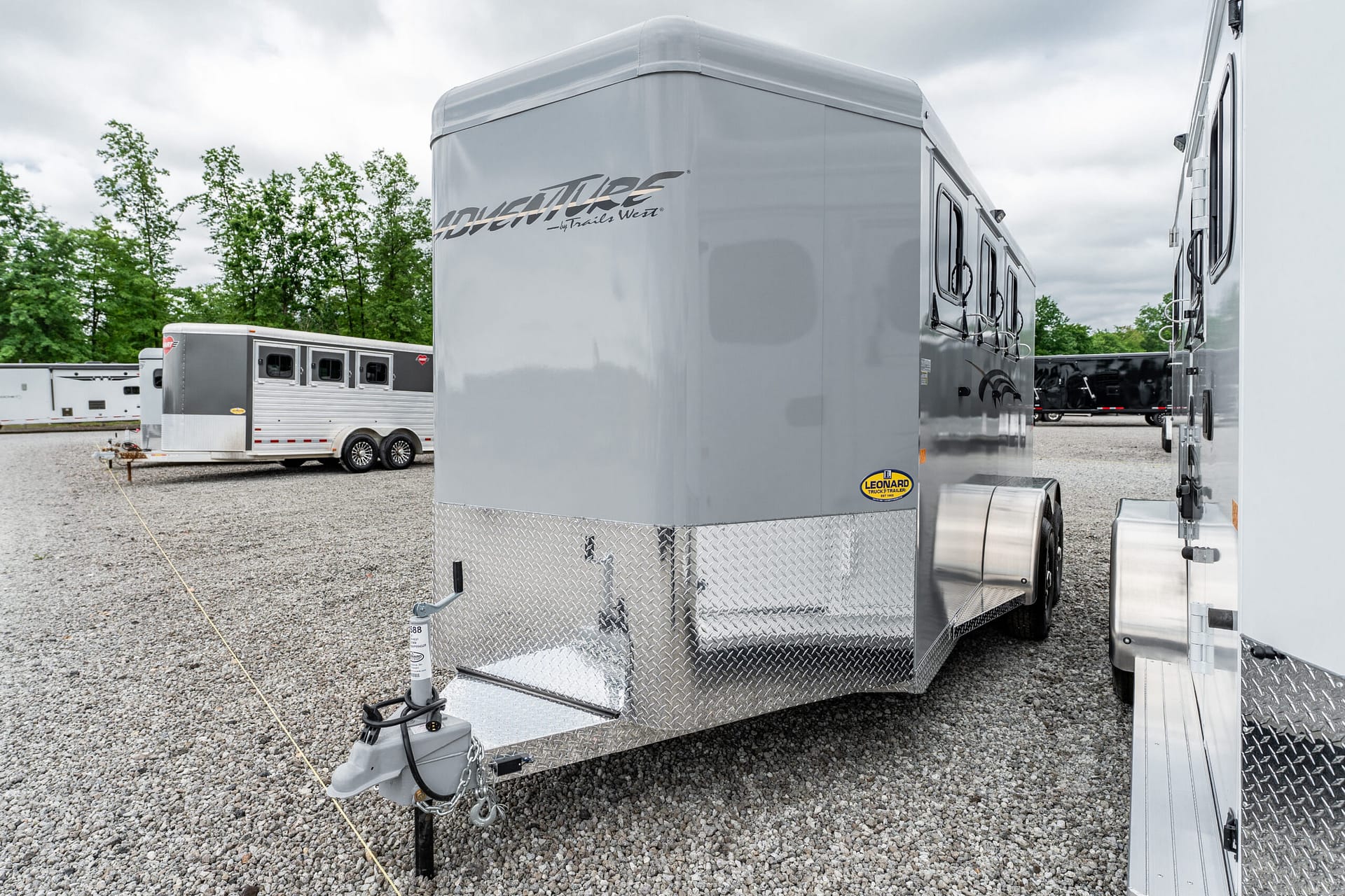 Large silver travel trailer with diamond-plate front, parked on a gravel lot among other trailers.