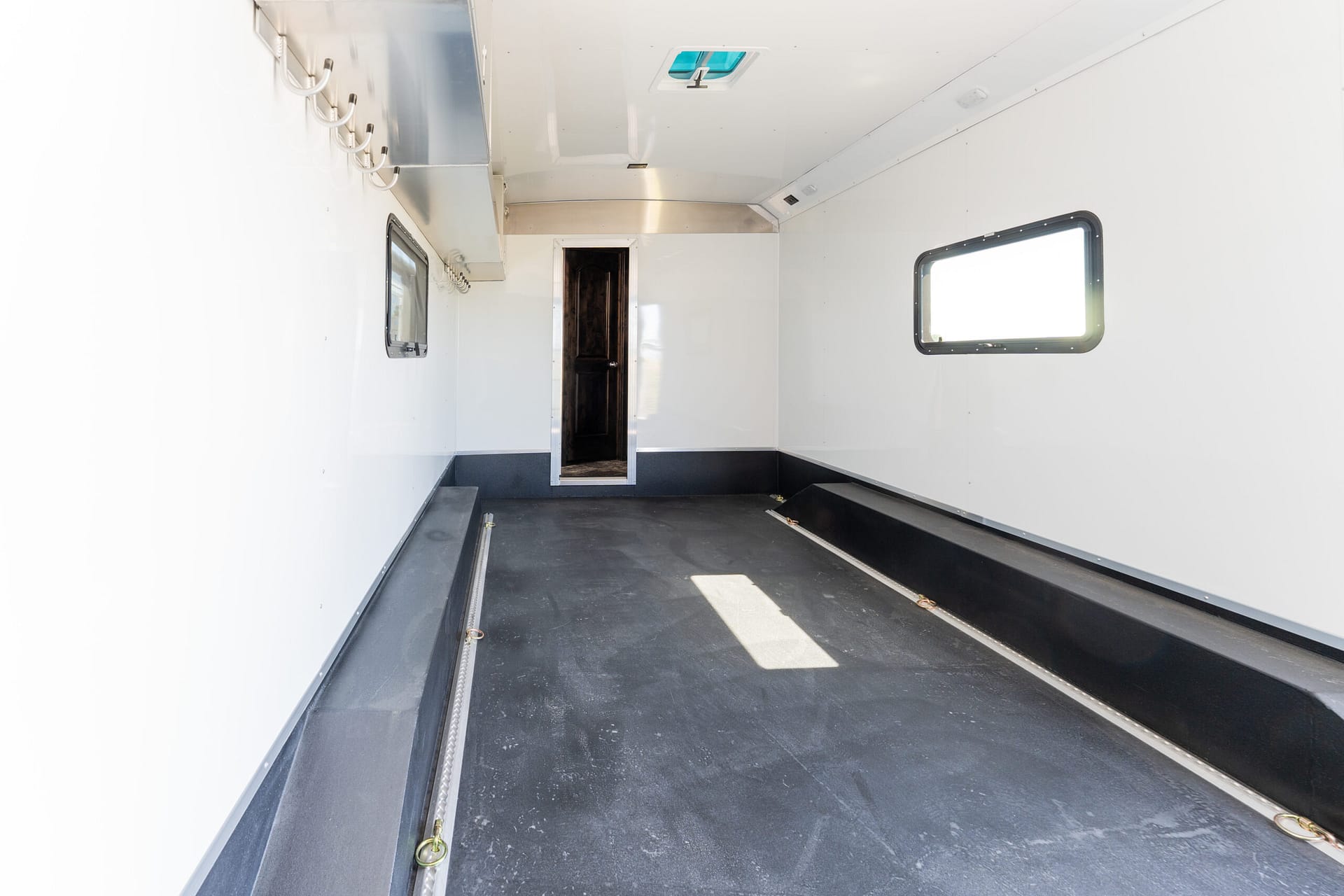Interior of a white trailer with a dark floor, hooks along the left wall, and a doorway at the far end