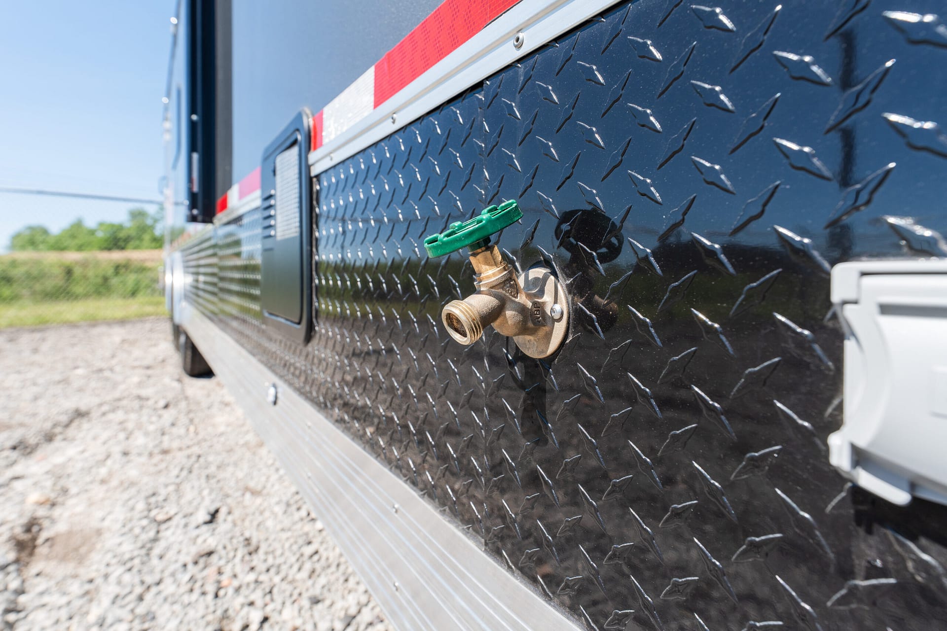 Close-up of a green valve on a diamond-plate metal side panel of a utility trailer.