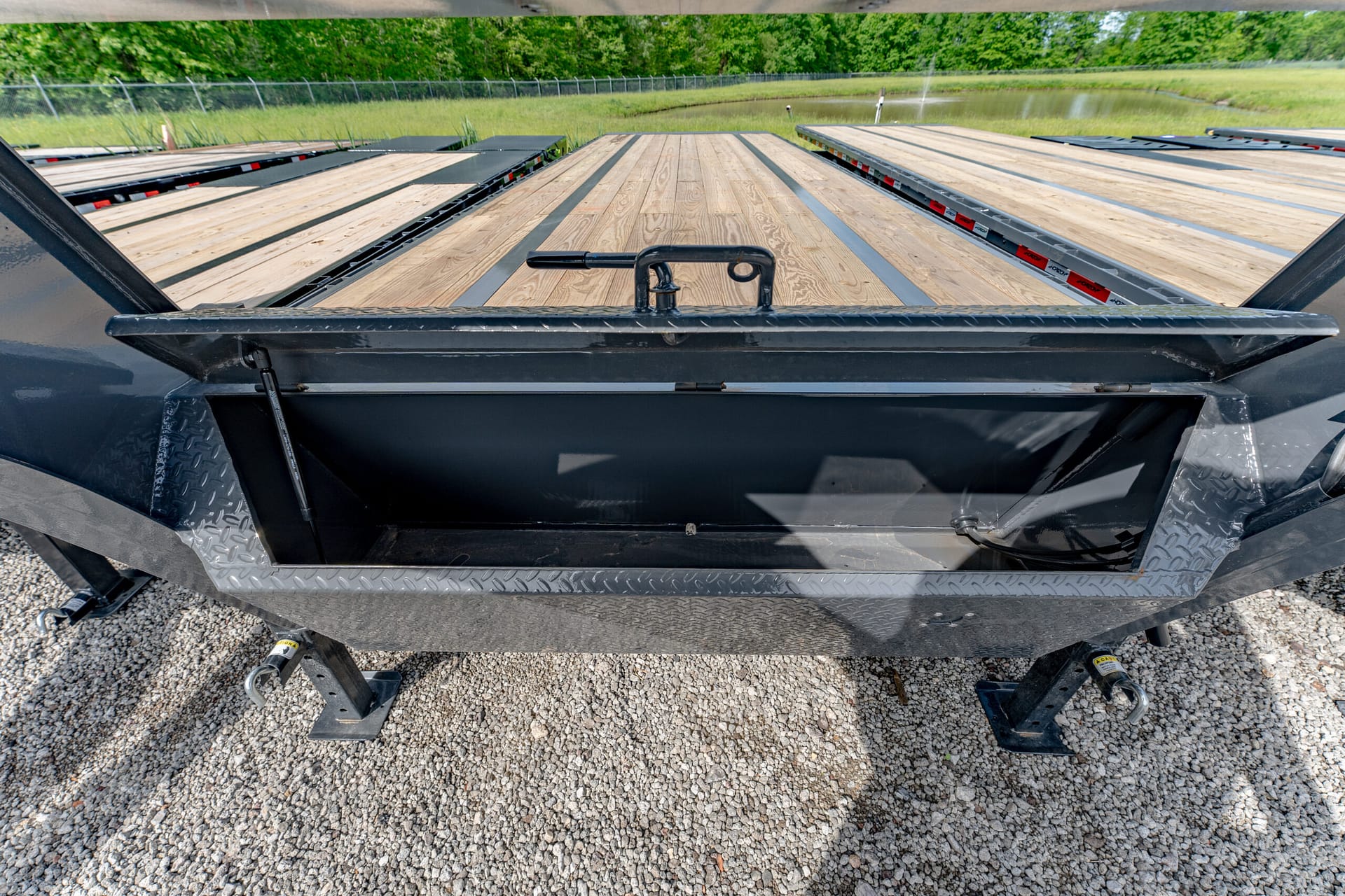 Rear view of a black flatbed trailer with a wooden deck, parked on gravel.