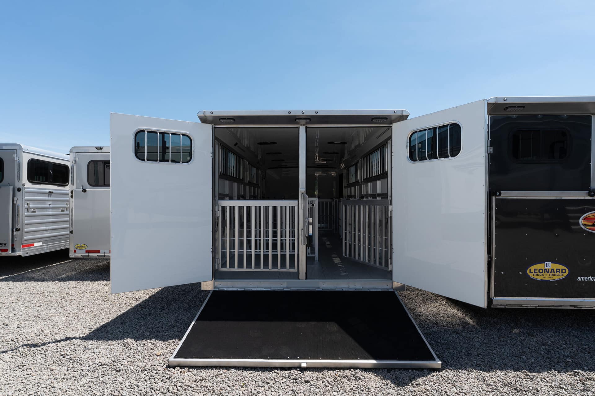 Open horse trailer with ramp down, showing interior stalls on a gravel lot under a clear blue sky