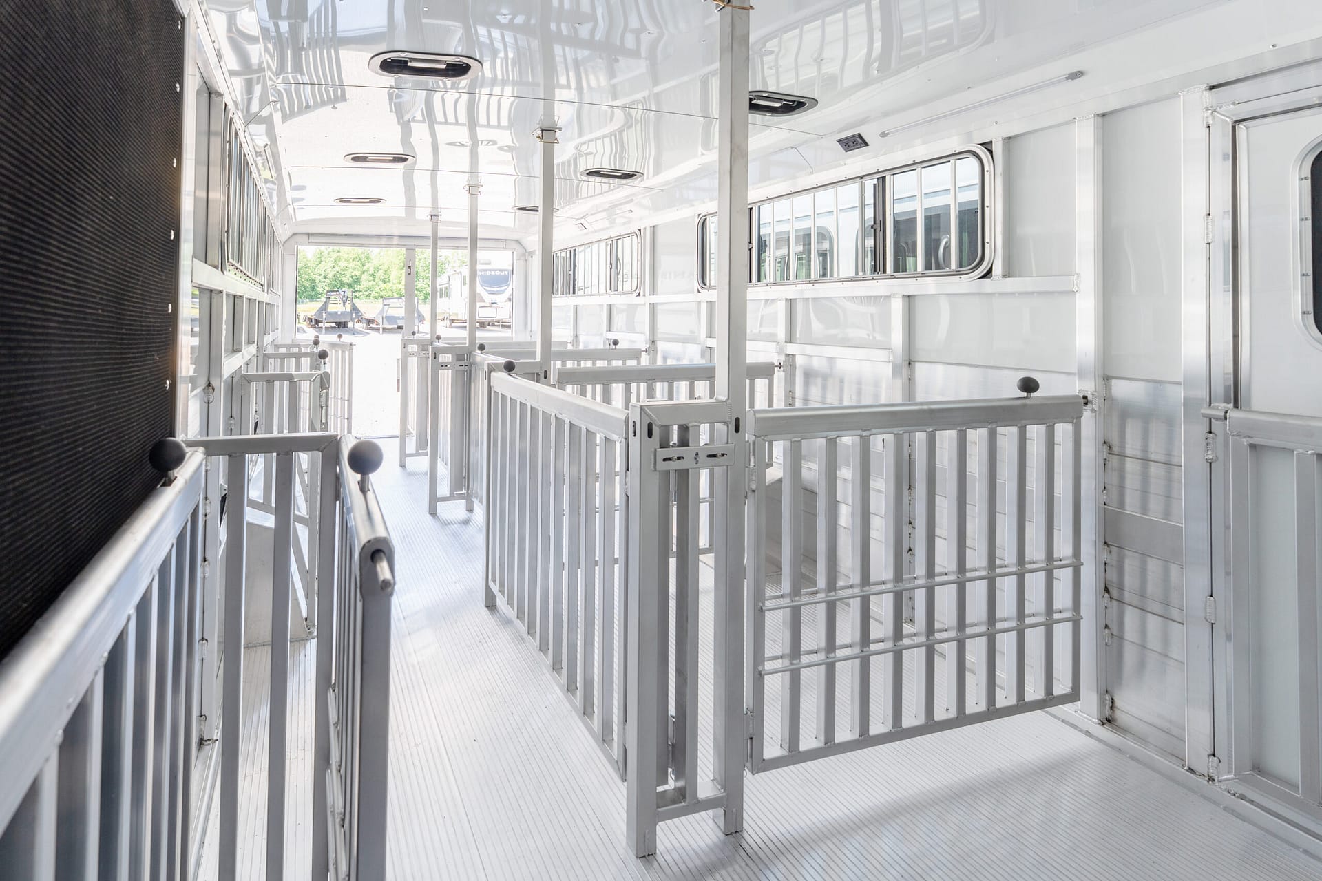 Interior of a silver aluminum livestock trailer with partition gates and side windows, daylight visible at the far end.